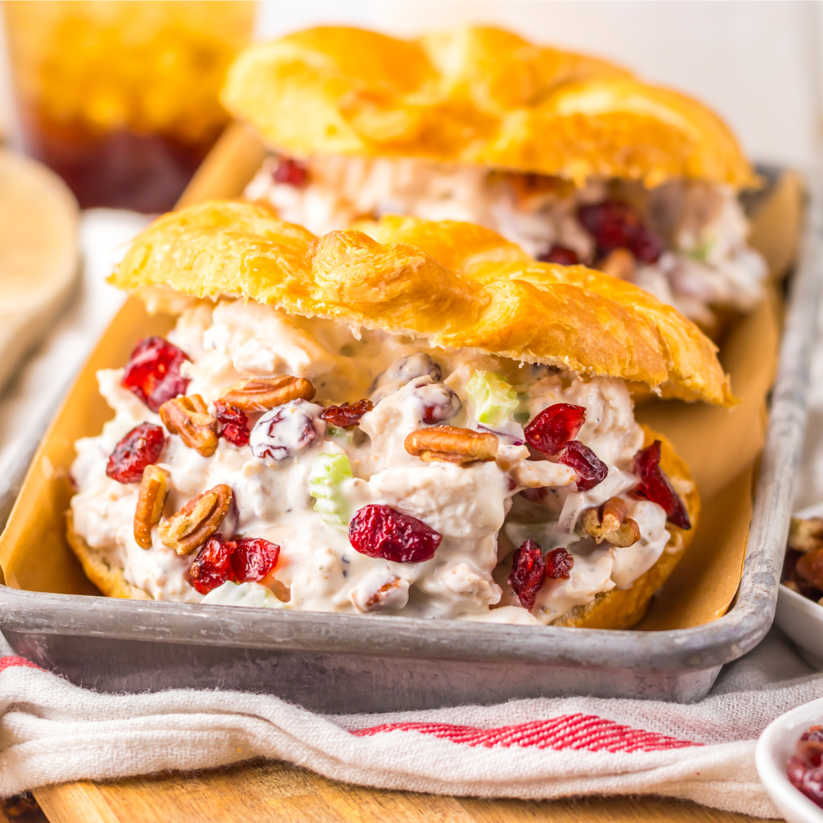 Close up view of a Cranberry Pecan Chicken Salad Croissant on a metal tray sitting on a red and white towel  .