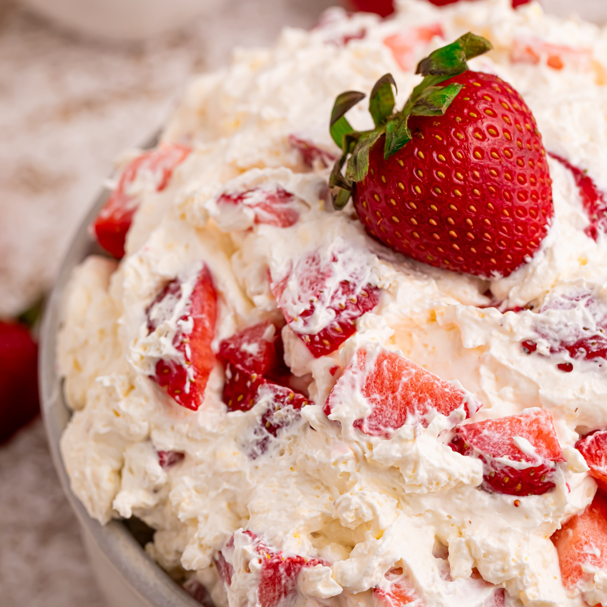 Close up view of the strawberry cheesecake salad in a white bowl with a fresh strawberry on top. 