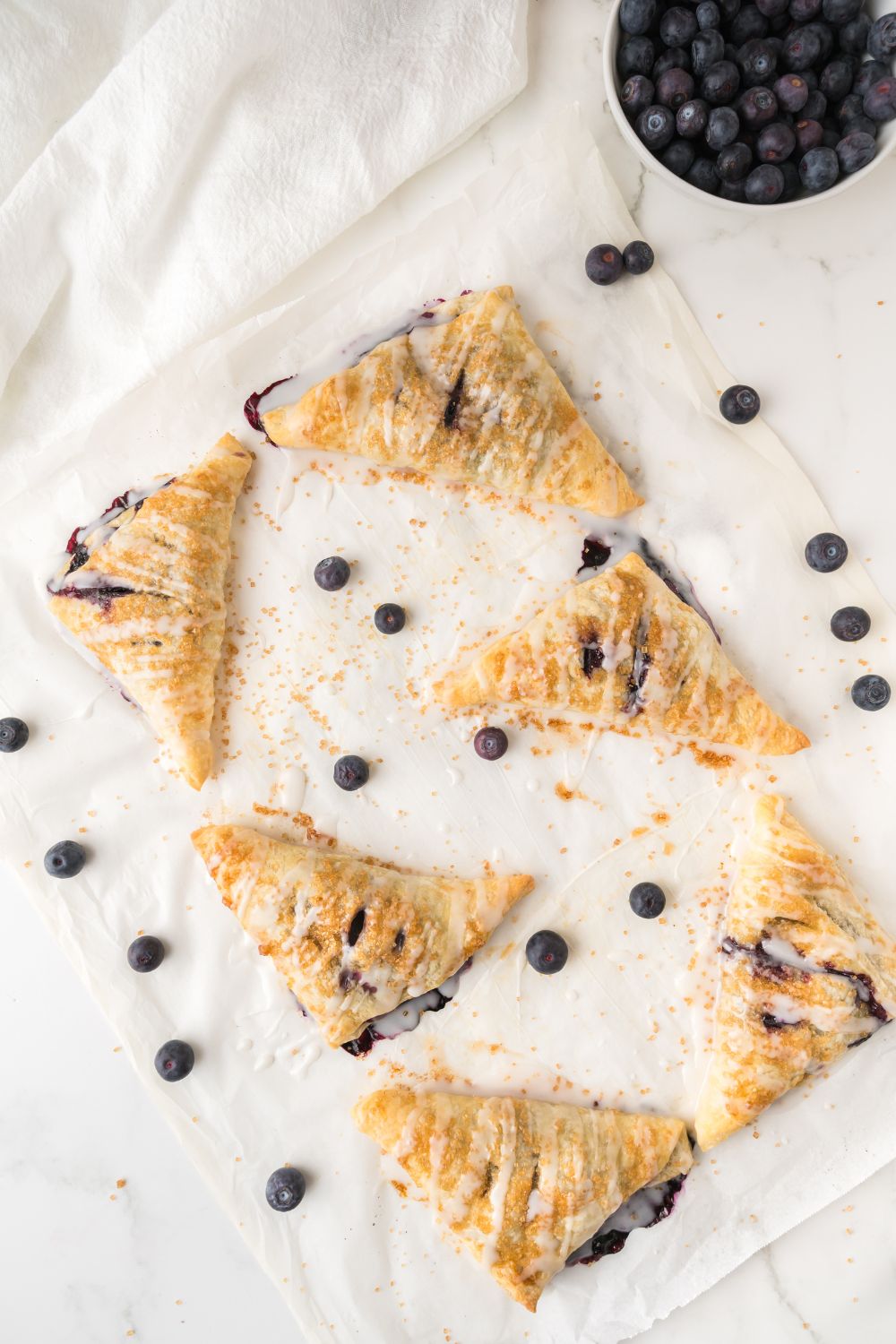 overhead view of Blueberry Turnovers on baking tray with a drizzle of glaze on top 