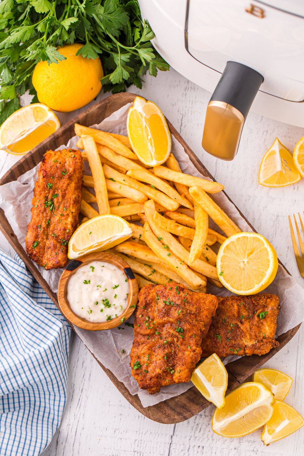 overhead look of Air Fryer Fish And Chips on a tray on table with lemons, parsley, and air fryer to side 