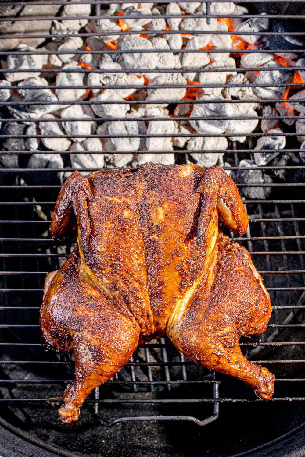 Smoked Whole Chicken sitting on a charcoal grill 