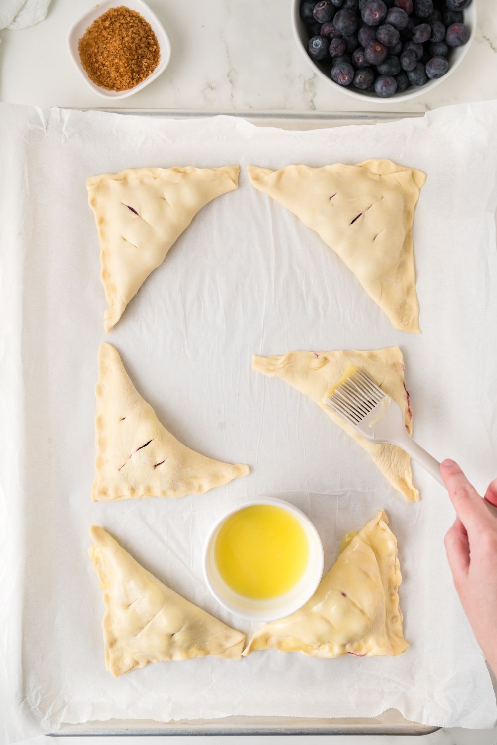 poking holes in pastry and a small bowl of butter to the side for Blueberry Turnovers