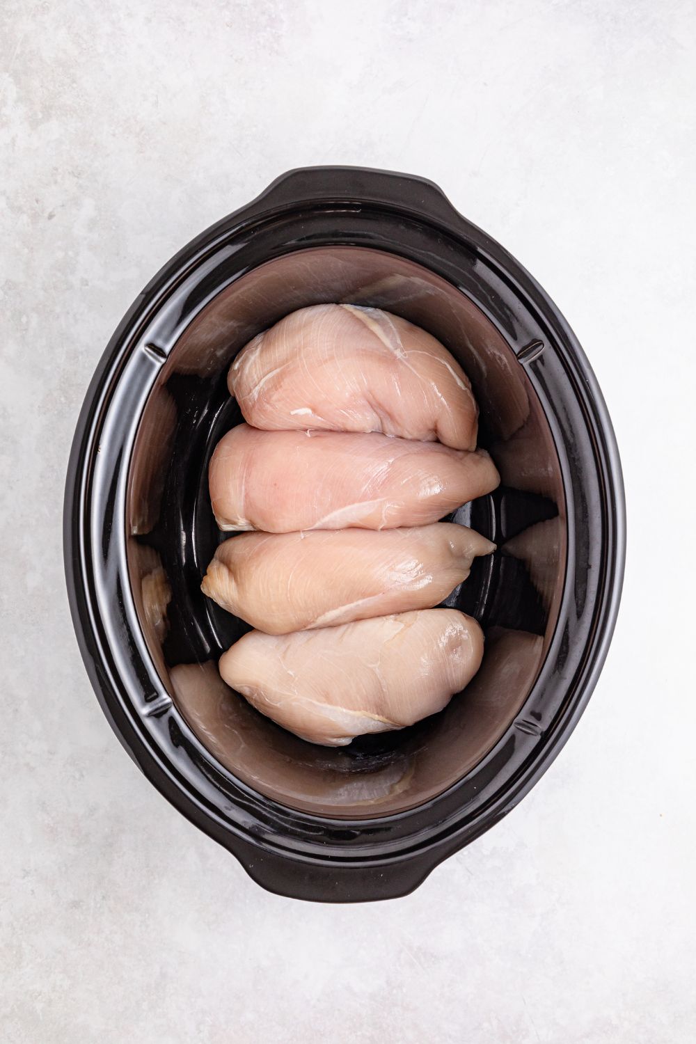 raw chicken breast in slow cooker on table 