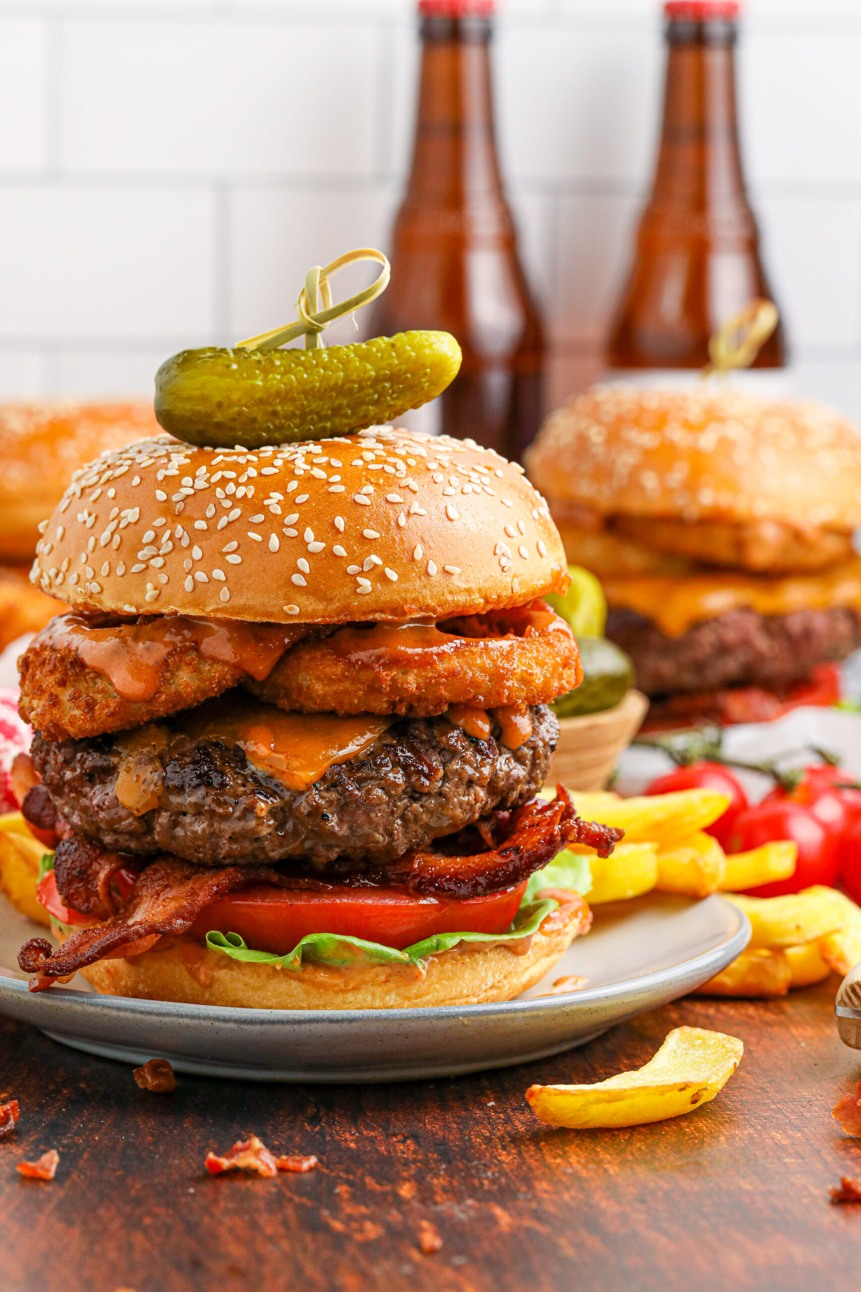 up close side view of the Cowboy Burger on a white plate that is fully loaded with toppings with a small pickle on top