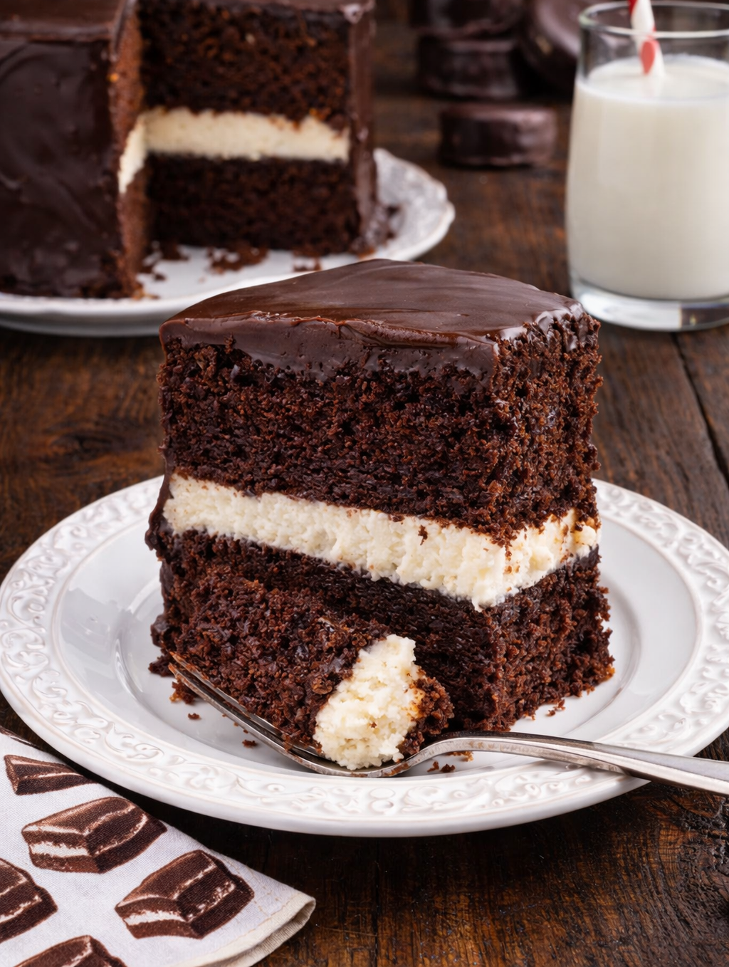 Slice of Ding Dong Cake on a white plate with the whole cake in the background 