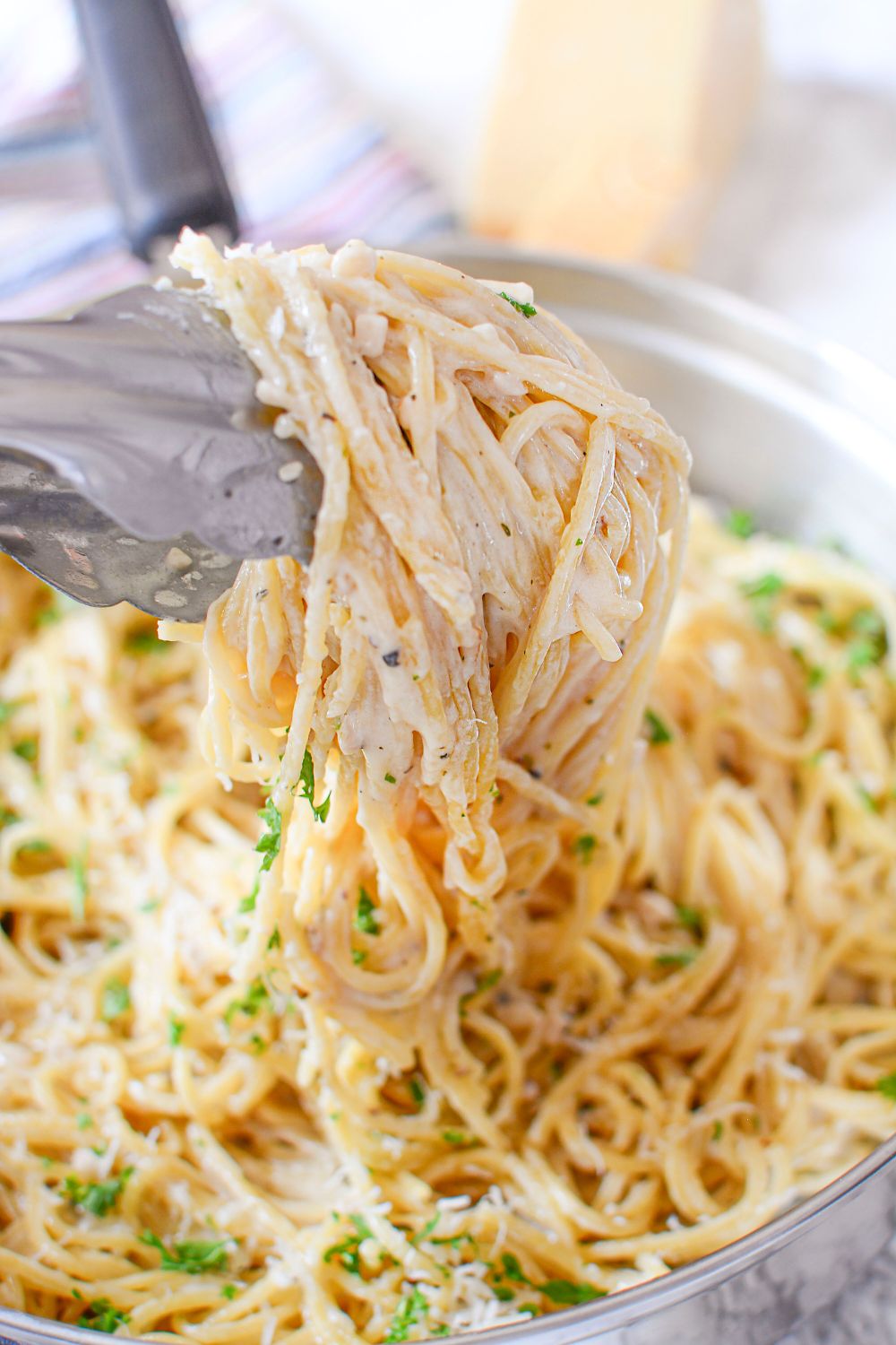 garlic parmesan pasta on tongs being lifted out of skillet