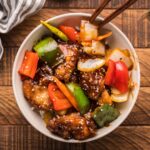 General Tso Chicken in a bowl with tongs on the side