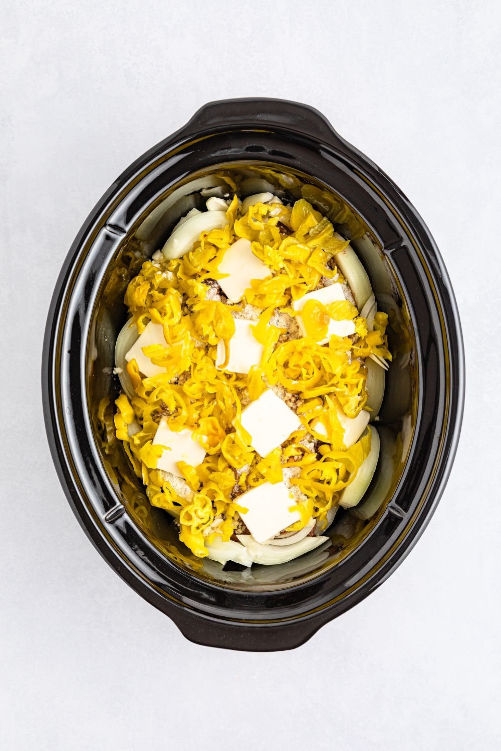 raw mississippi roast in slow cooker topped with peppers and slabs of butter 