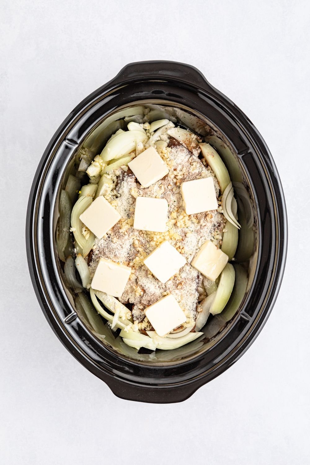 seasonings and butter on top of pot roast in a slow cooker 