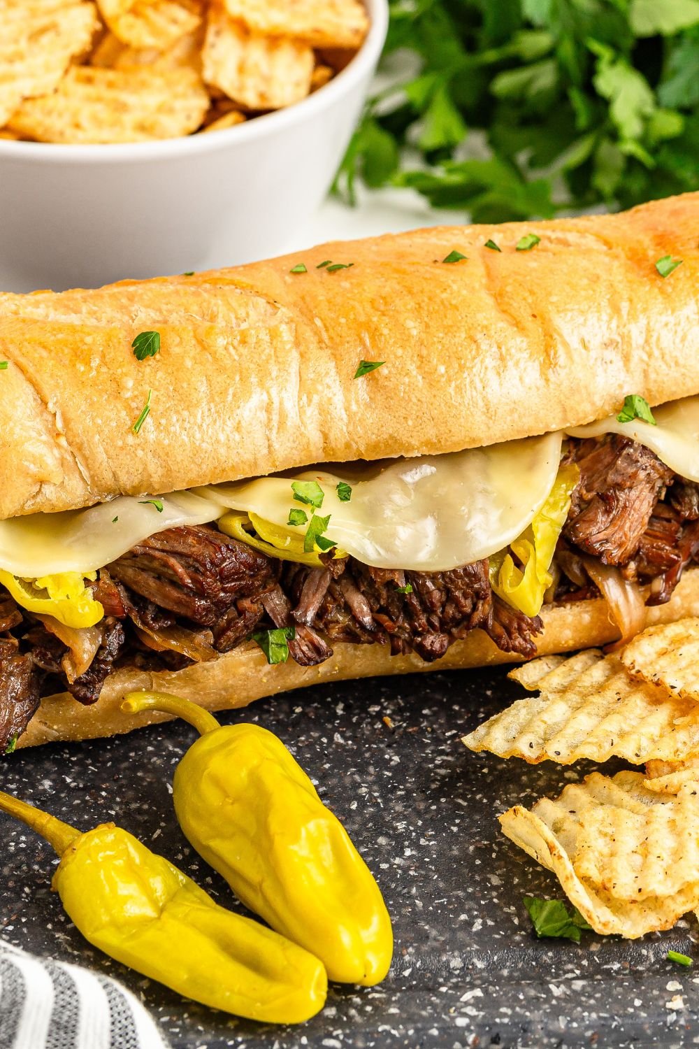 Mississippi Pot Roast Sandwich on table with some chips and peppers in front of sandwich 