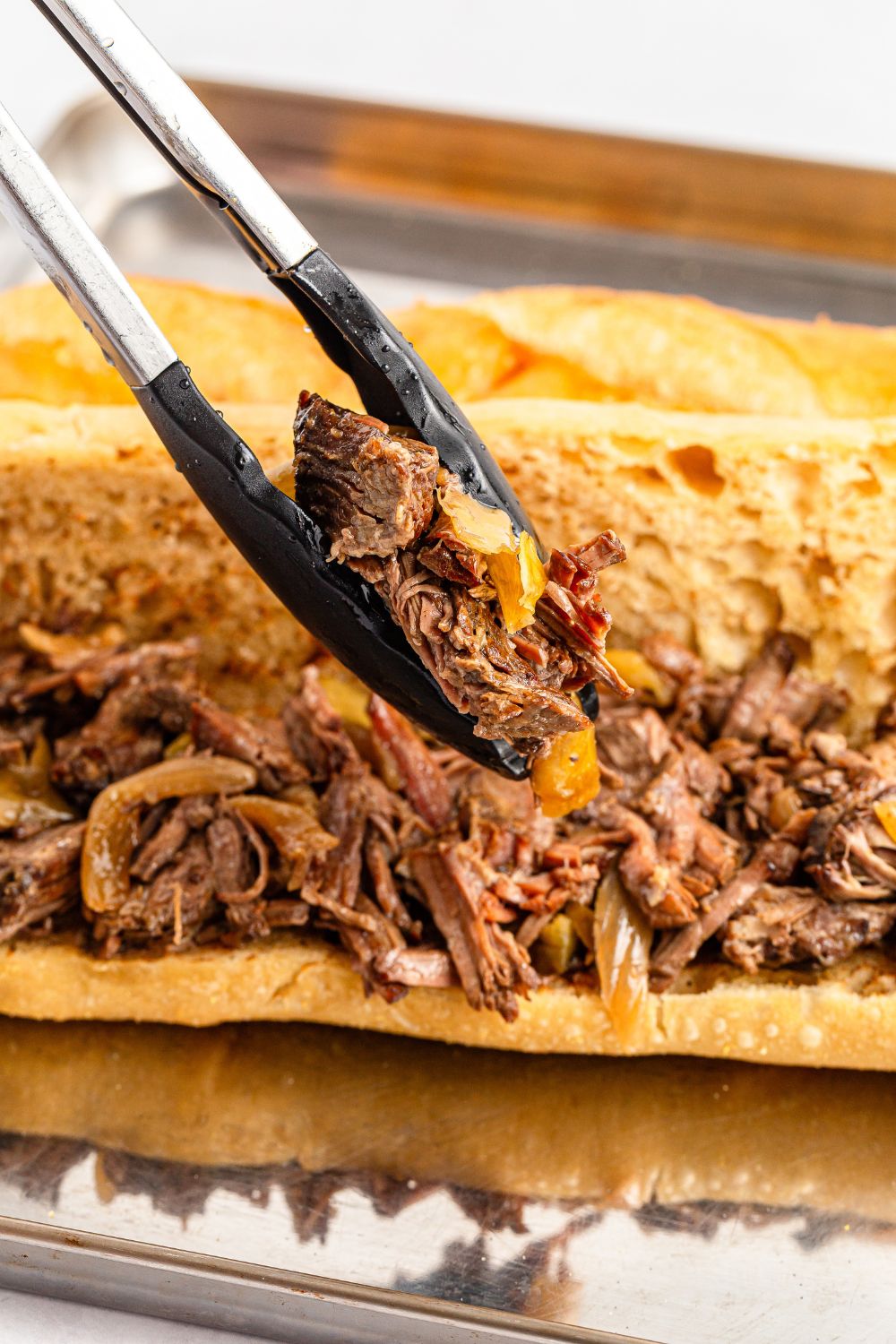 Mississippi Pot Roast Sandwich with tongs putting more meat in sandwich 