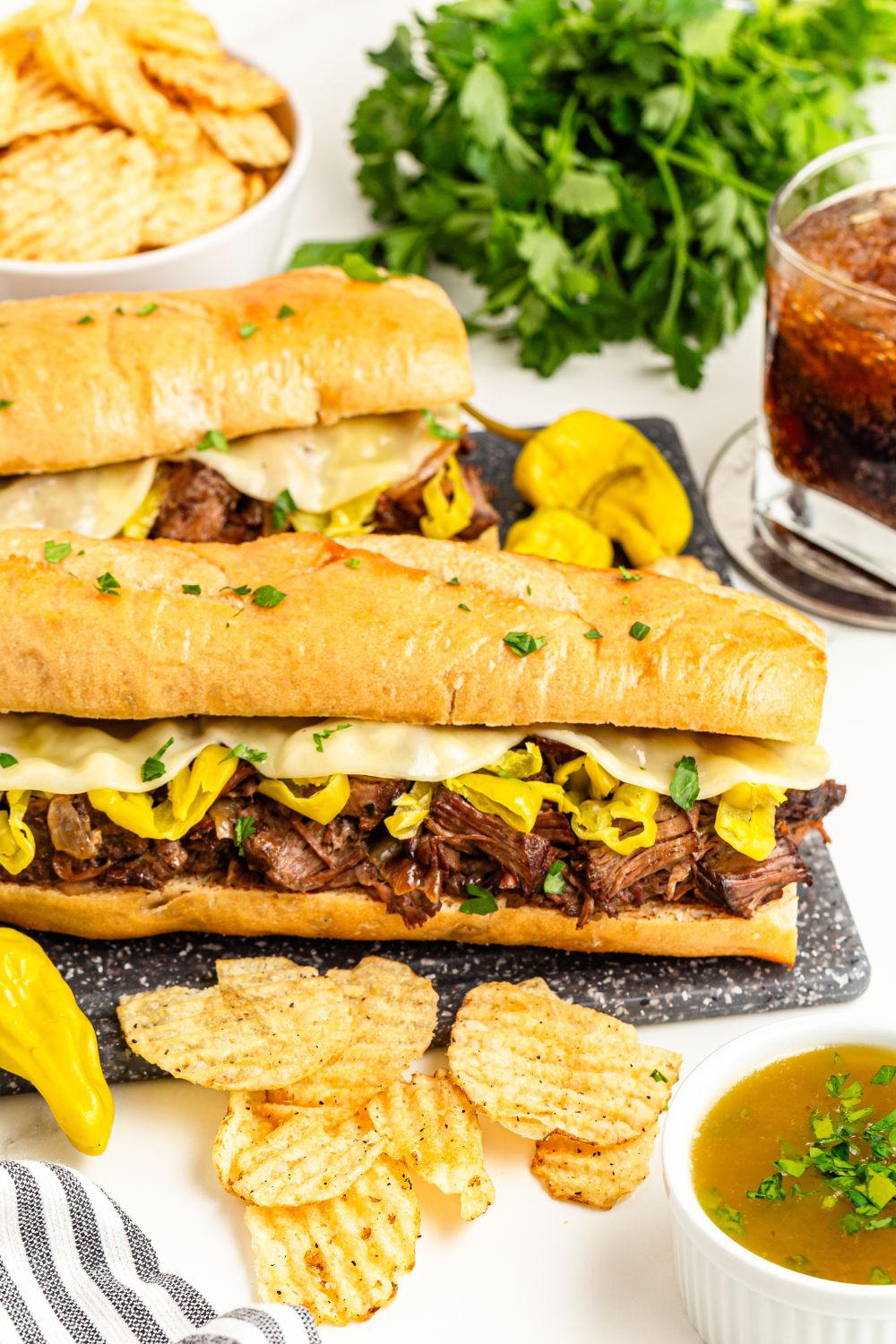 Mississippi Pot Roast Sandwiches on a plate with chips, parsley, and drink to the side