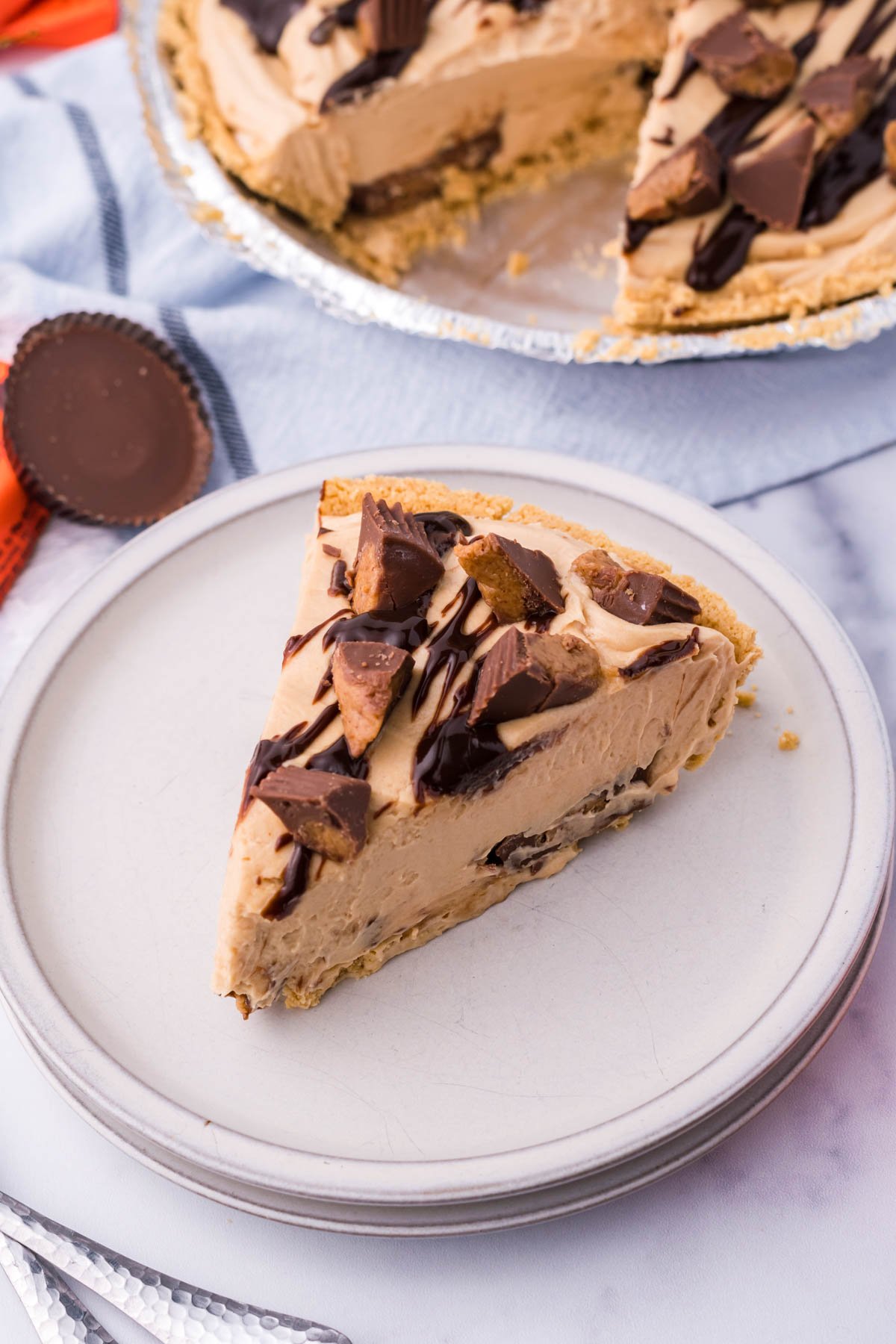 A top view of a slice of no bake peanut butter cup pie on a white plate with the full pie in the background. 