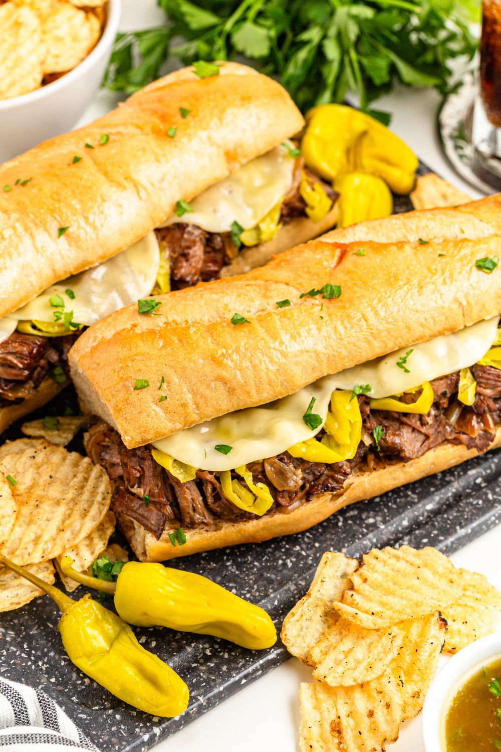 mississippi beef sandwiches and peppers on table with some chips and a bowl of au jus on side