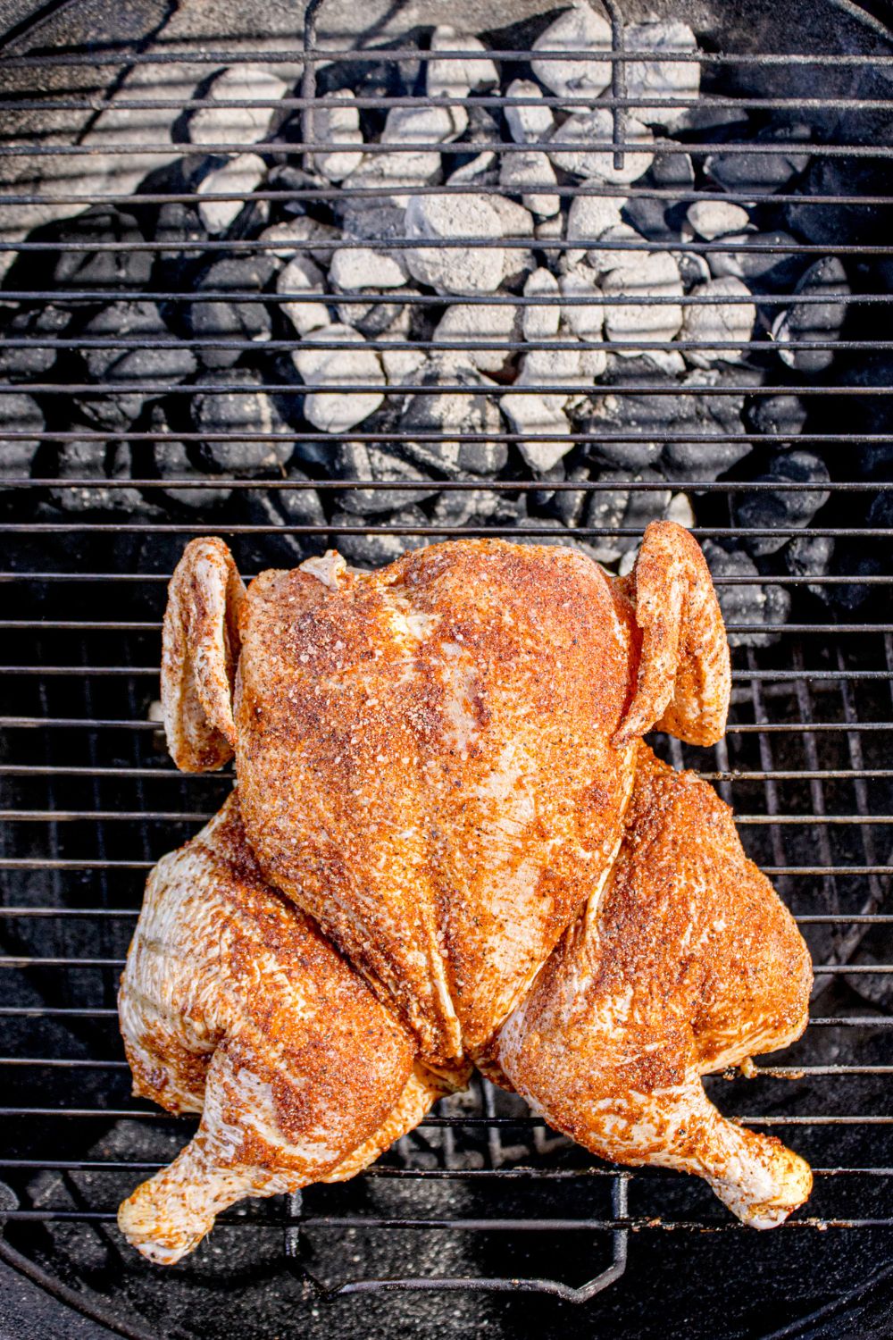 raw Smoked Whole Chicken sitting on a charcoal grill 