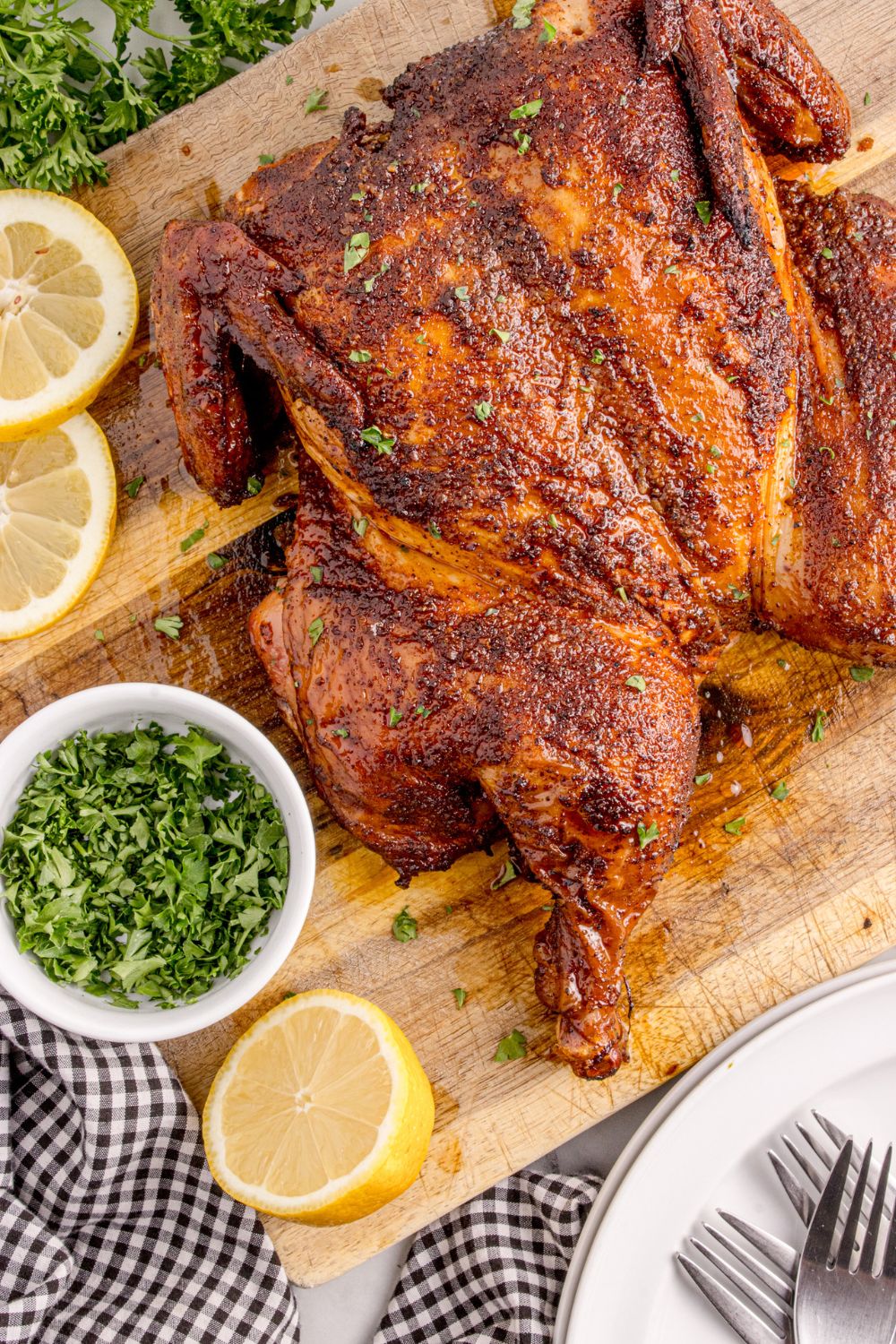 Smoked Whole Chicken on a cutting board with lemon and herbs in a small bowl 
