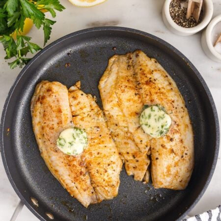 Pan Fried Tilapia in a skillet with lemon butter on top and lemon on side