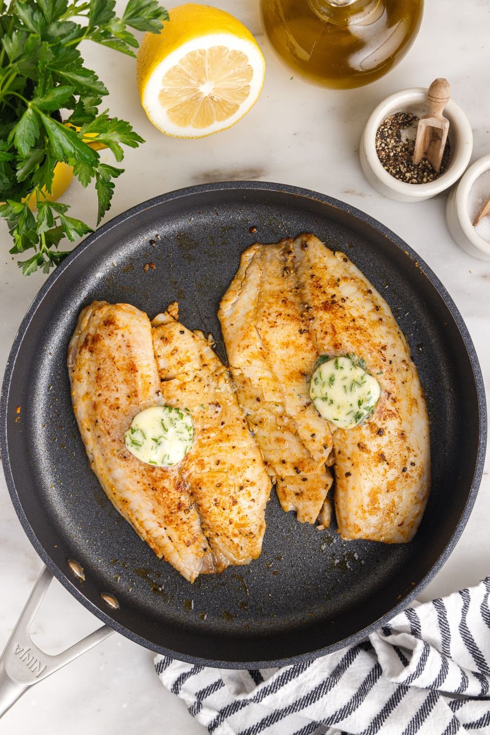 Pan Fried Tilapia in a skillet with lemon butter on top and lemon on side 
