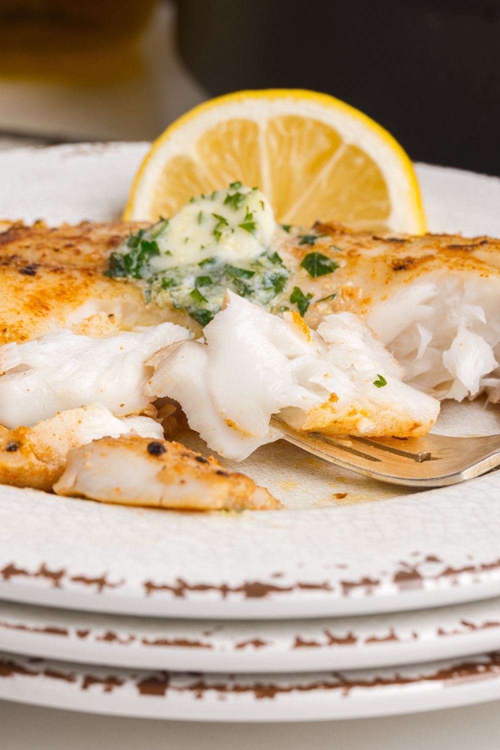 Pan Fried Tilapia on plate with a lemon wedge on side 