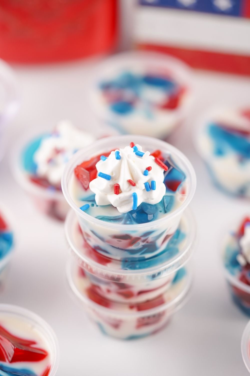 Red White and Blue Jello Shots stacked on top of one another on table with flag in background 
