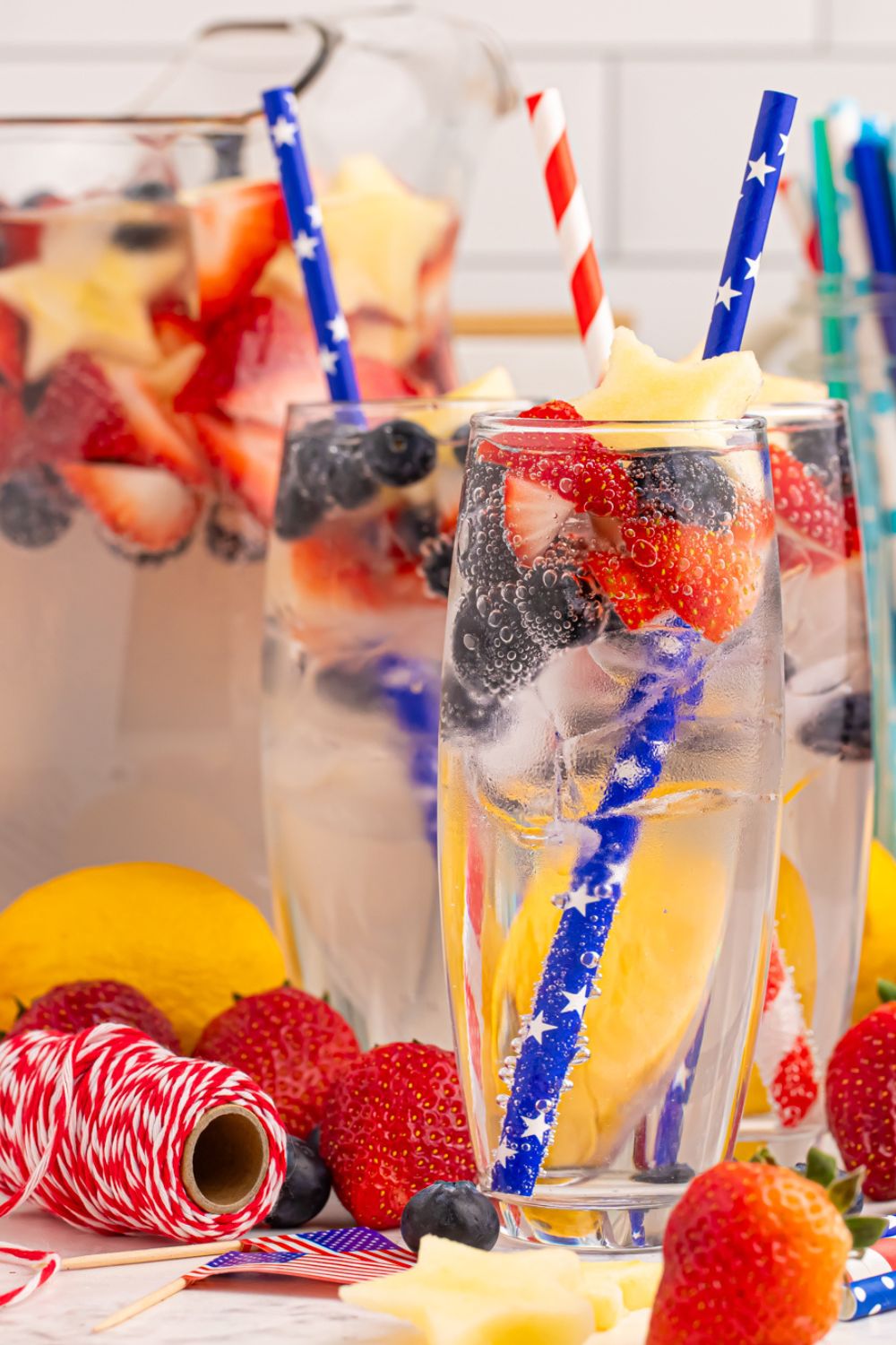 Patriotic Sparkling Lemonade in glasses and pitcher full of lemonade. All glasses are garnished with fruit