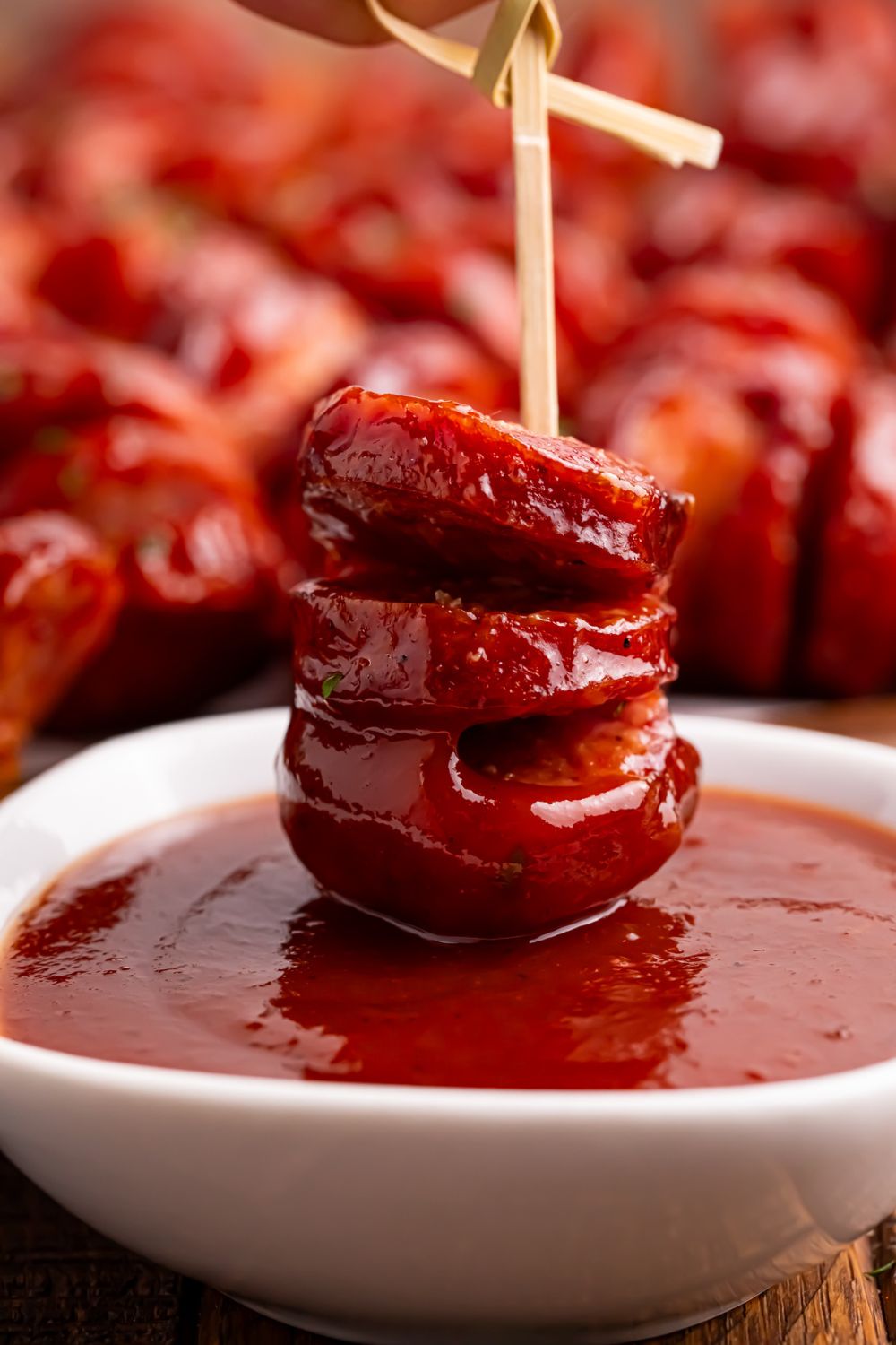 BBQ Hasselback Smoked Sausages dipped in sauce in a bowl 