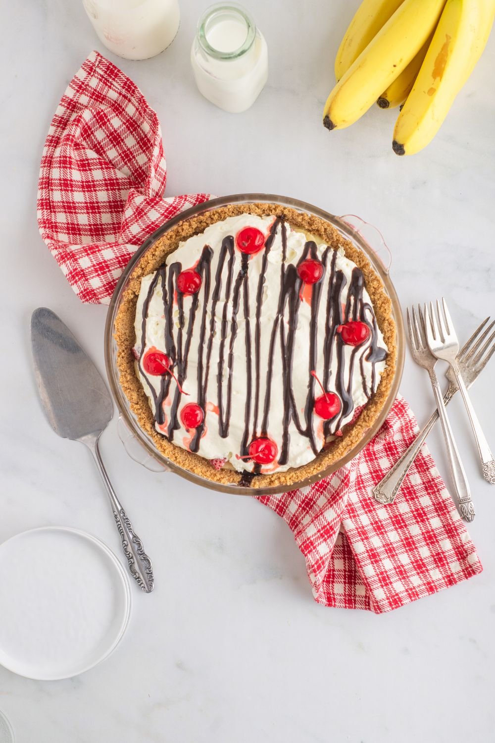 No Bake Banana Split Pie on table with forks to side, pie scoop, and more around the table 