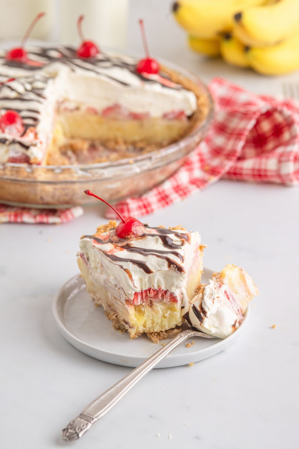 No Bake Banana Split Pie on table with a slice on a plate with a bite taken out of it 