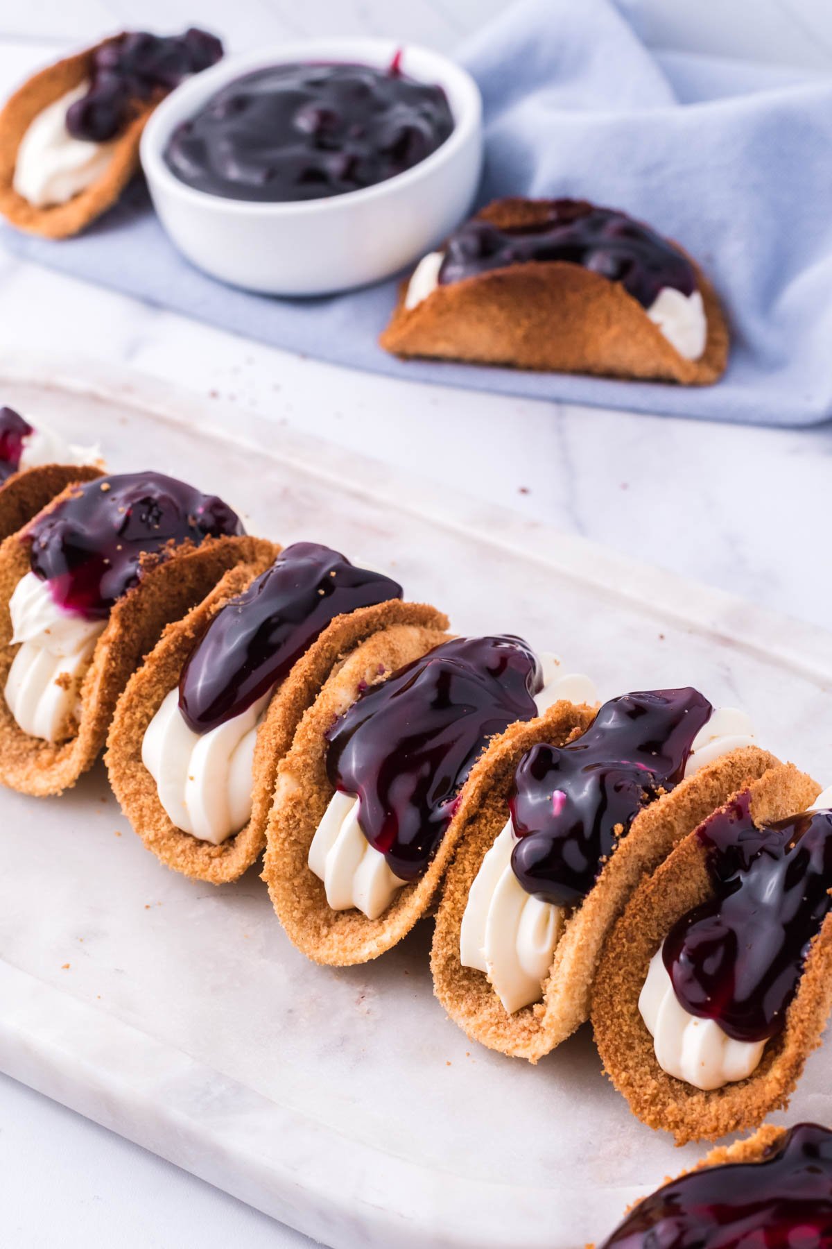 Photo of blueberry cheesecake tacos lined up on a marble serving platter. 