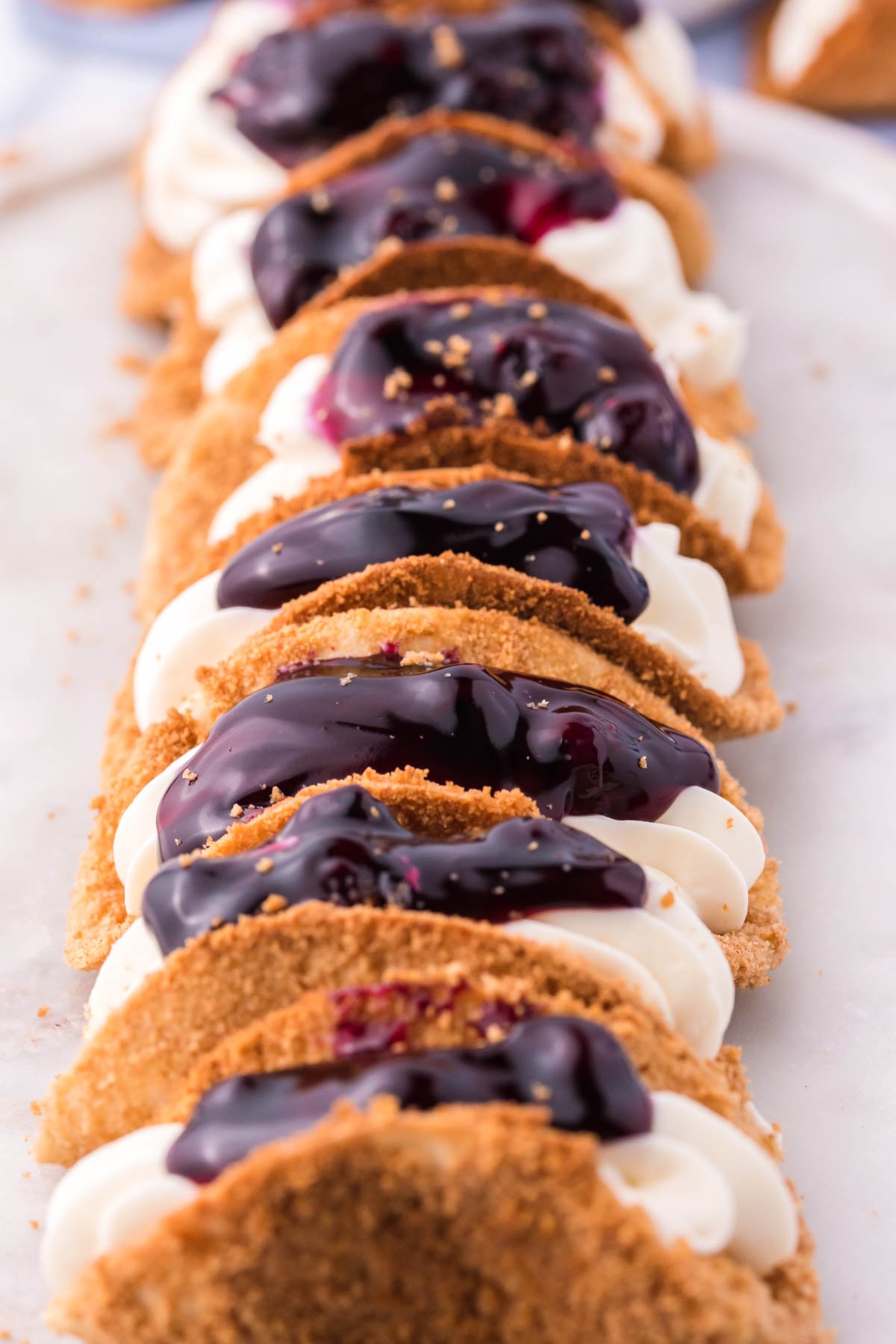 Photo of blueberry cheesecake tacos lined up on a marble serving platter. 
