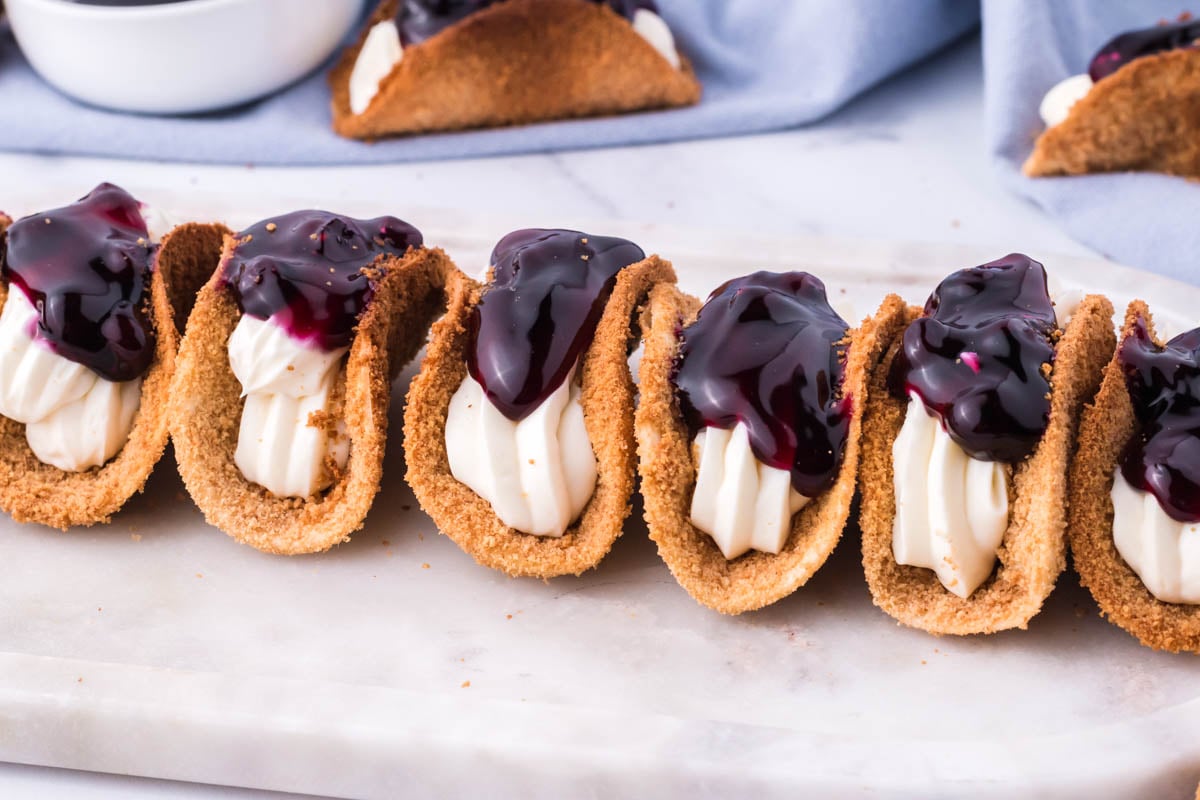Photo of blueberry cheesecake tacos lined up on a marble serving platter. 