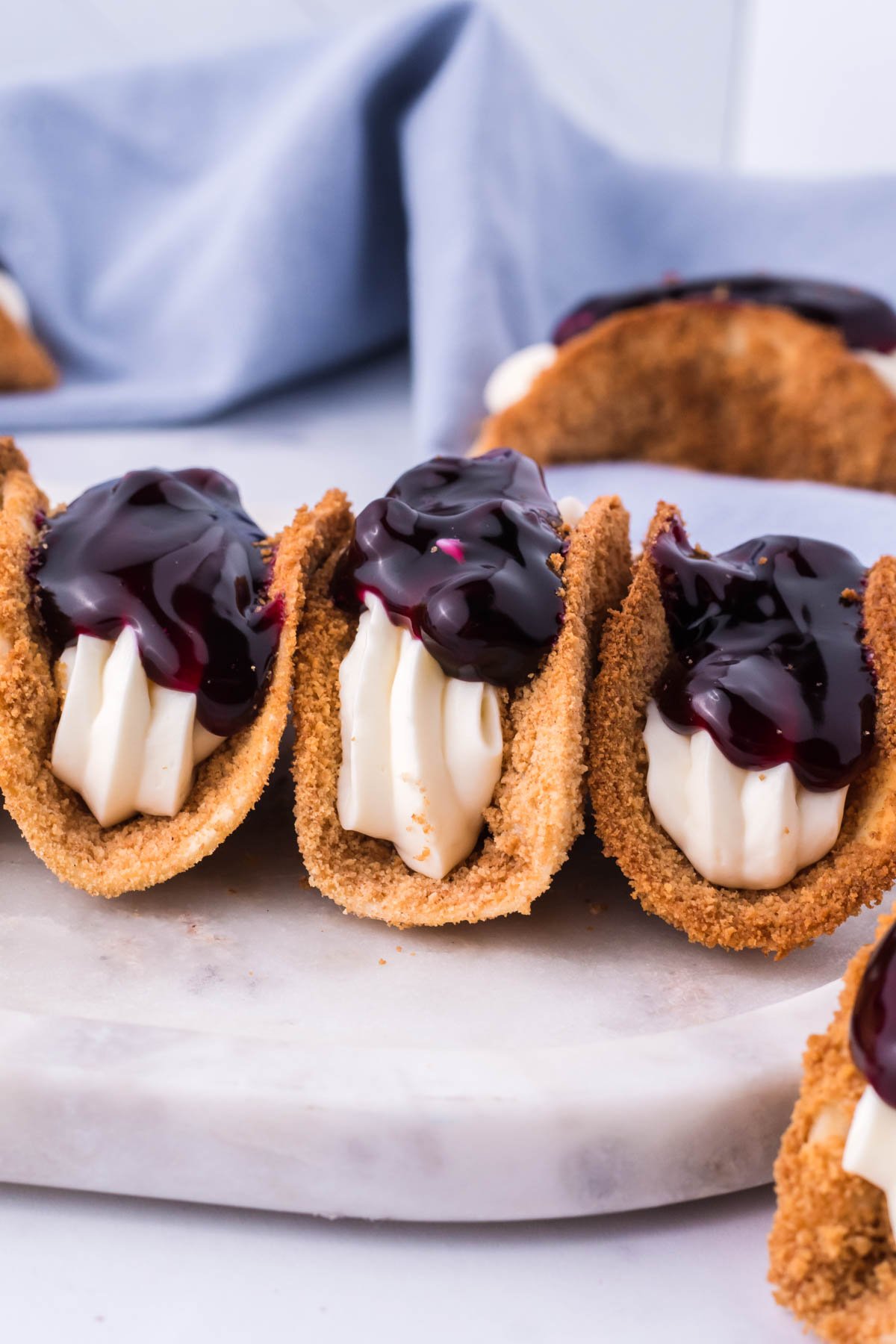 Photo of blueberry cheesecake tacos lined up on a marble serving platter. 