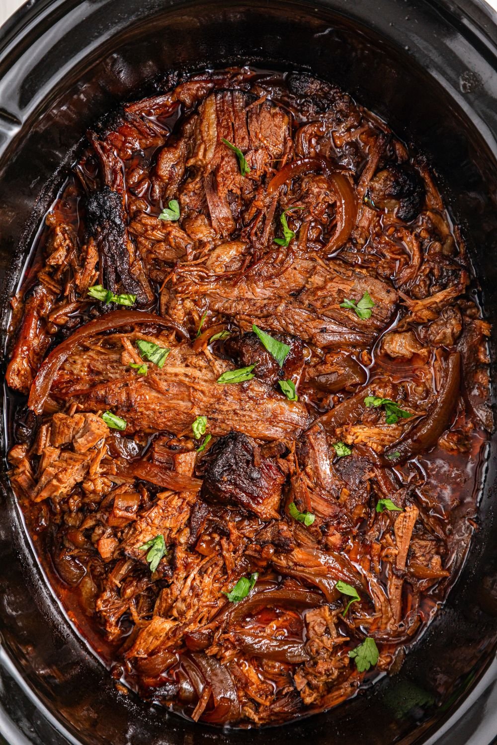 overhead shot of slow cooker full of bbq brisket topped with parsley 
