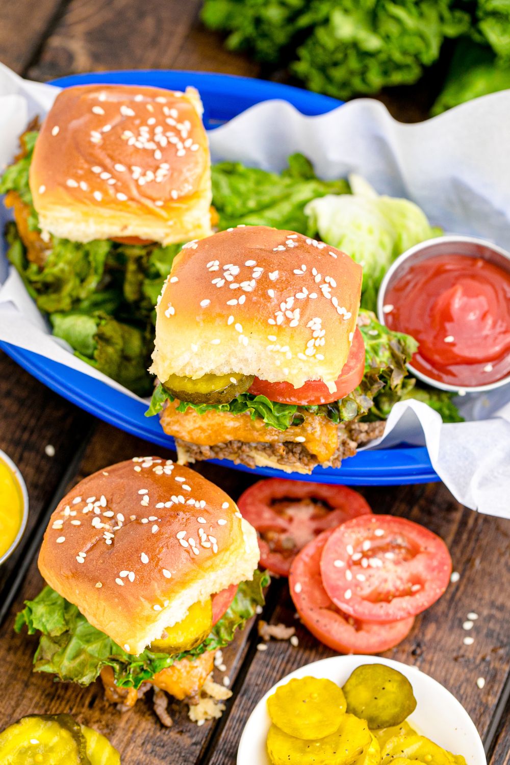 cheesy beef sliders loaded with toppings stacked on table and a basket on table
