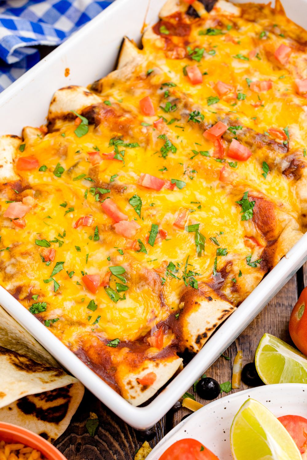 Cheesy Chicken Enchiladas in a casserole dish on table with some lime wedges on table 