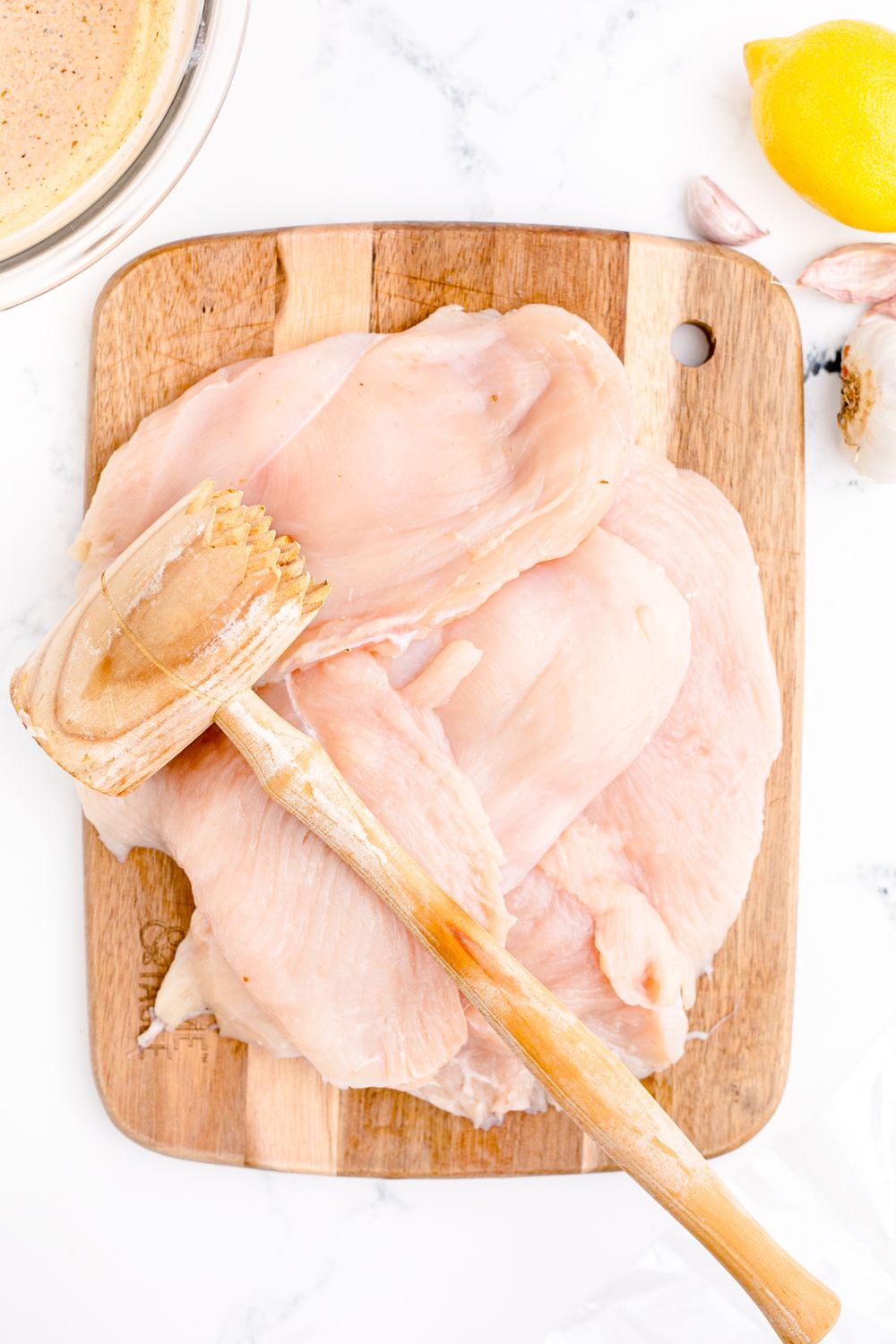 mallet sitting on top of raw chicken on cutting board 