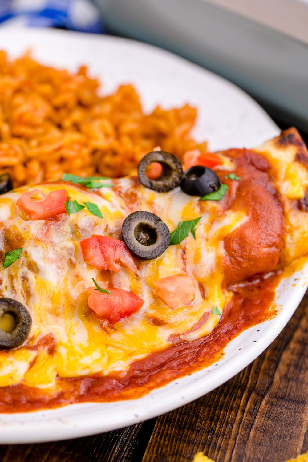 side view of plate that is topped with a loaded chicken enchilada and some seasoned rice 