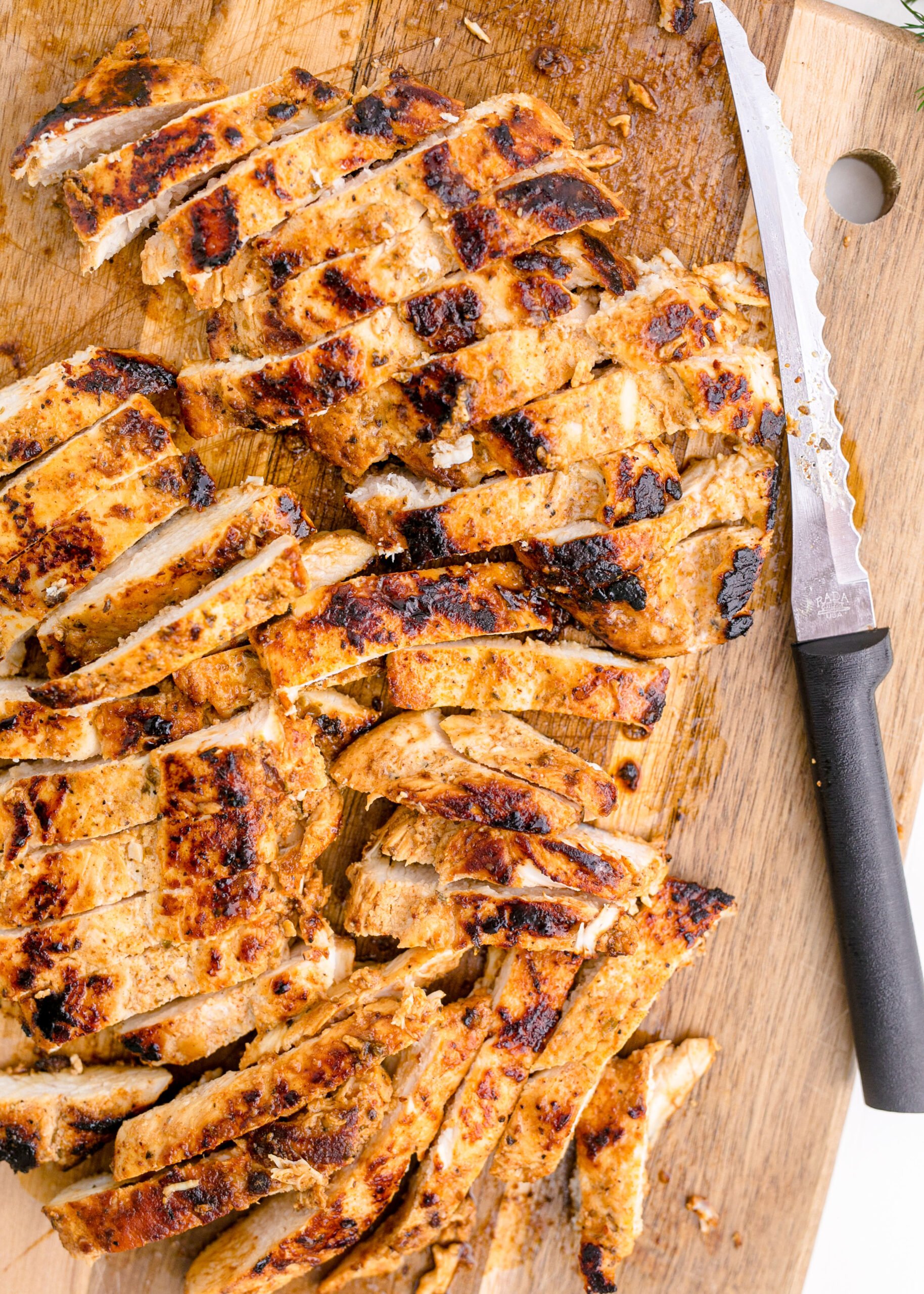 Chicken on a wooden cutting board being sliced up by a sharp knife