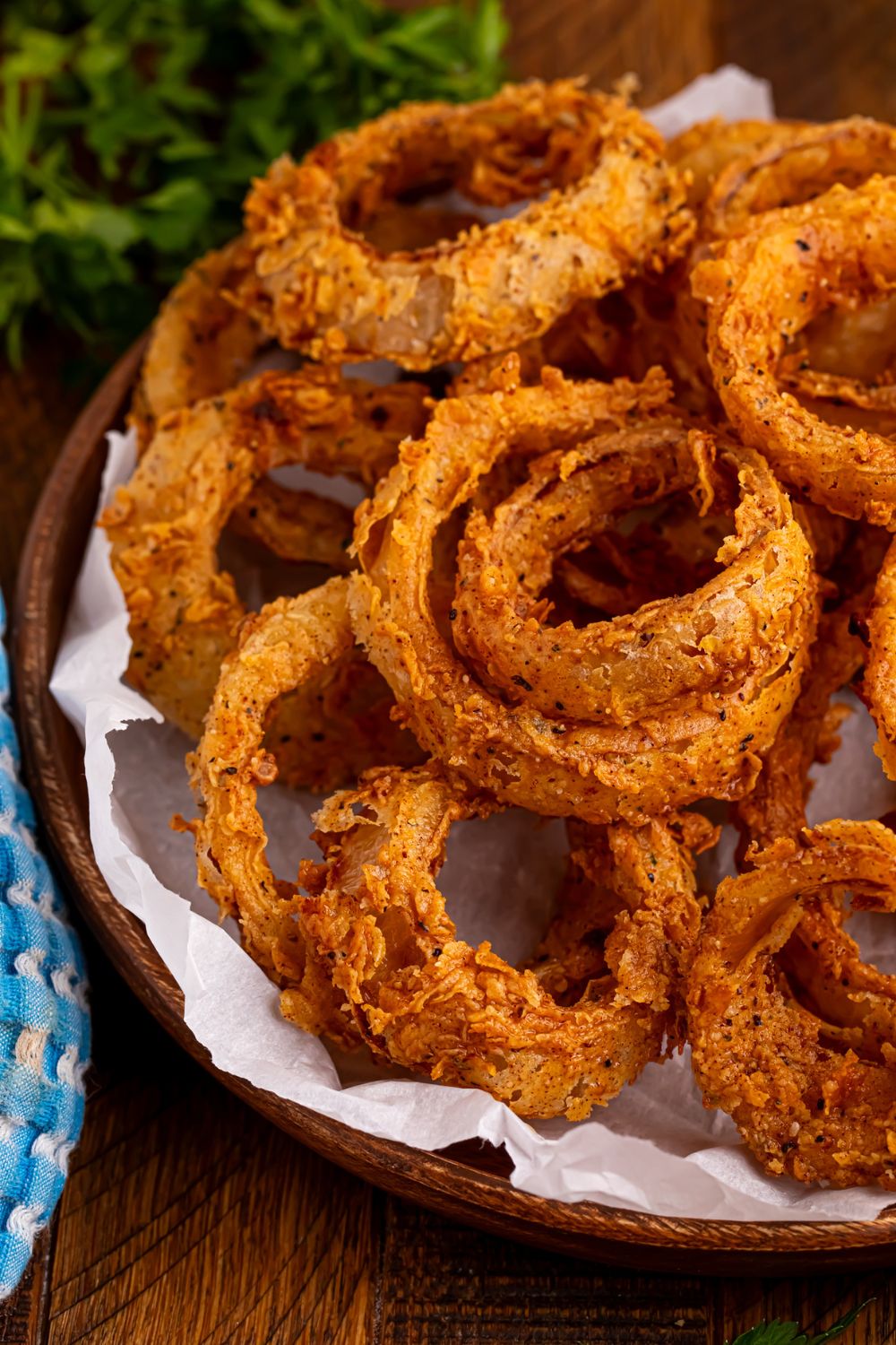 Homemade Deep Fried Onion Rings in a tray with some parchment paper and some parsley behind it 