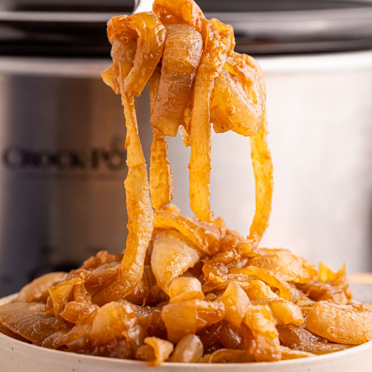 CrockPot Caramelized Onions in a bowl with the CrockPot behind it on table