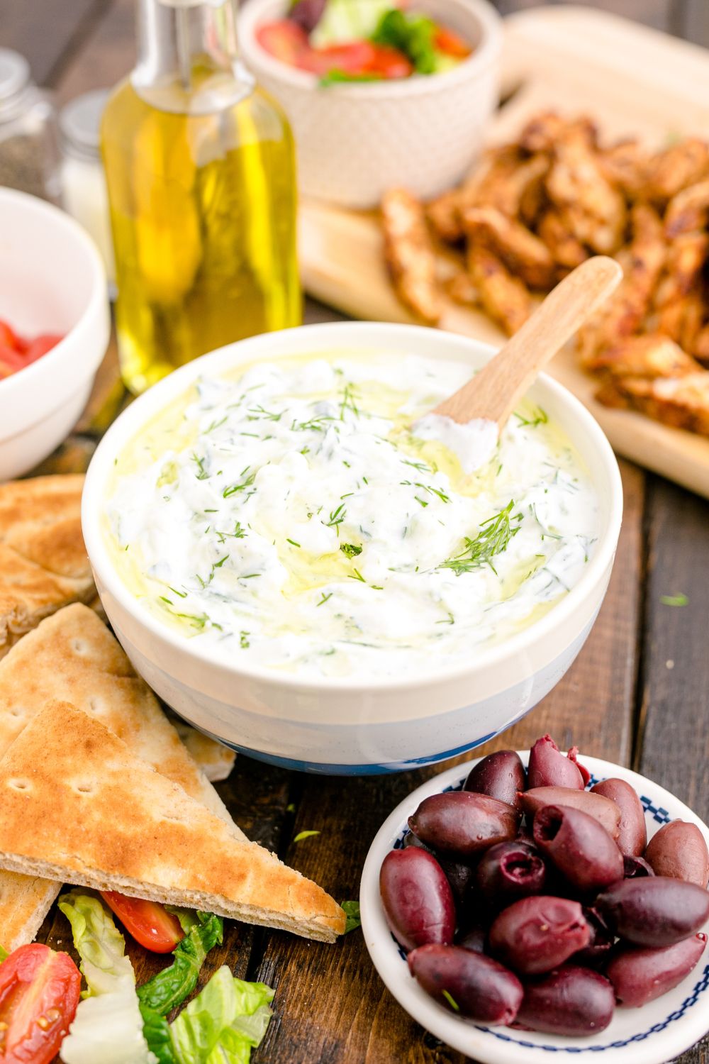 Tzatziki Sauce in a ceramic bowl with pita bread, olives and more around the bowl for dipping 