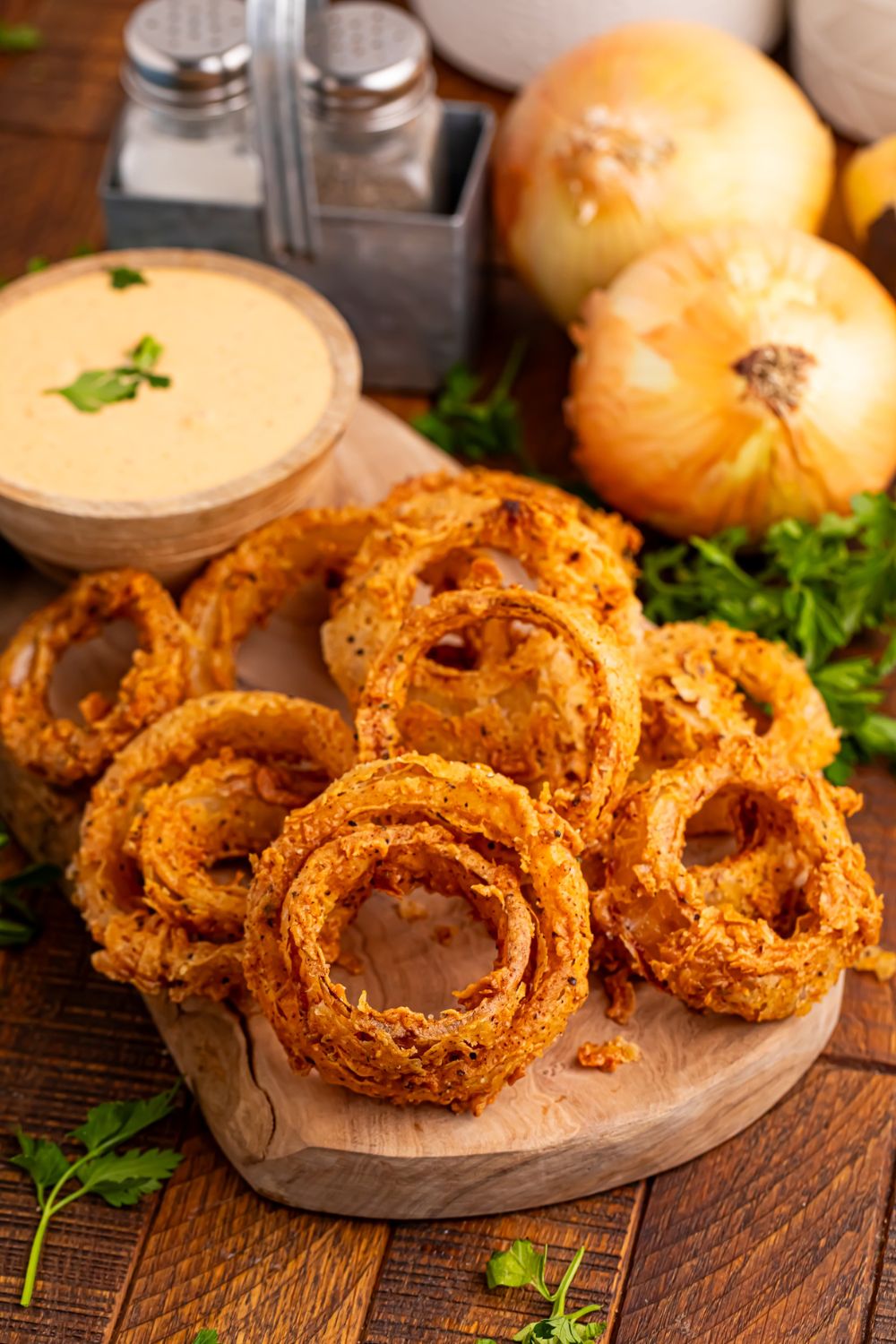 Homemade Deep Fried Onion Rings on a cutting board with whole onions behind it on table 