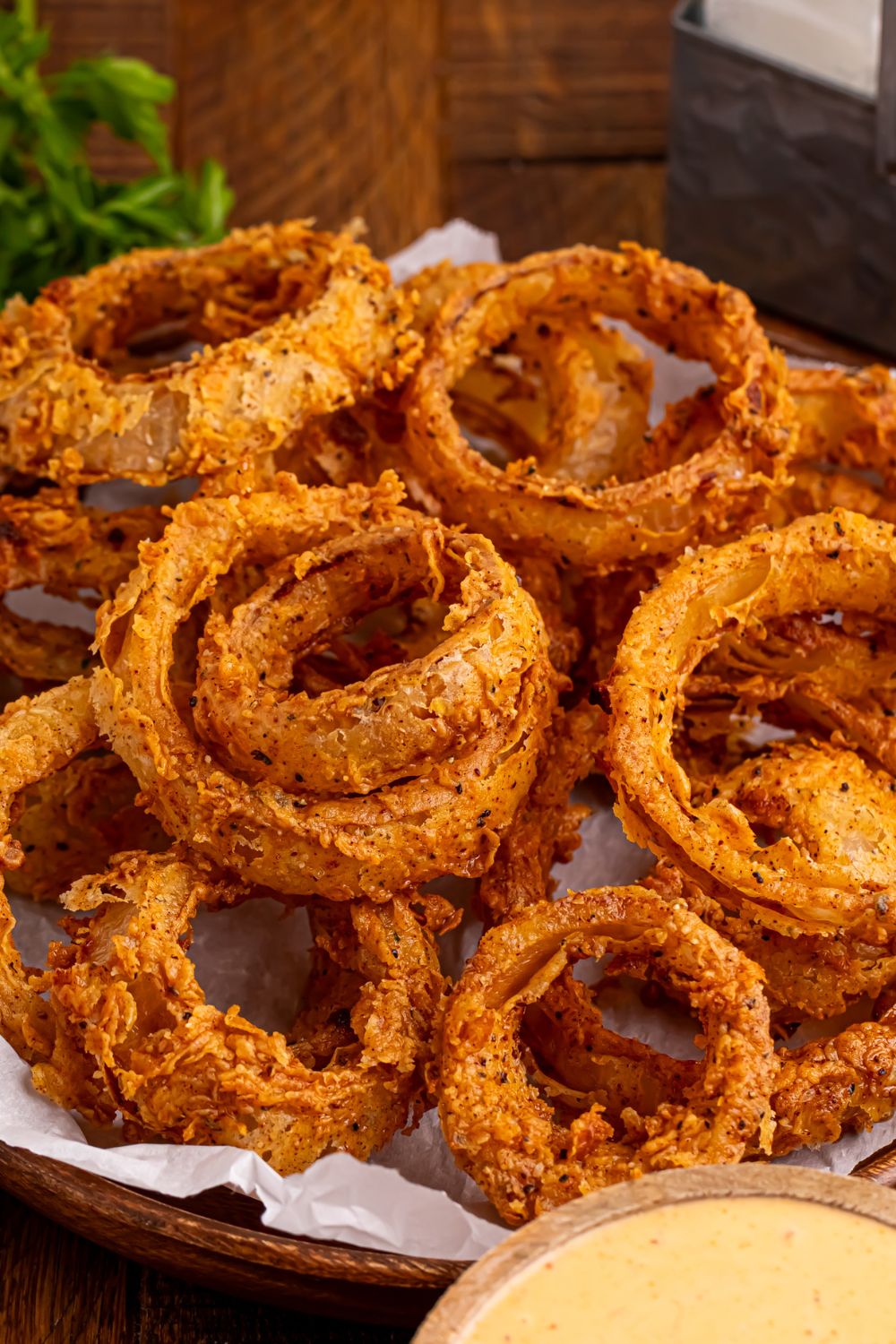 Homemade Deep Fried Onion Rings piled into a plate on table with a dipping sauce in a bowl in front