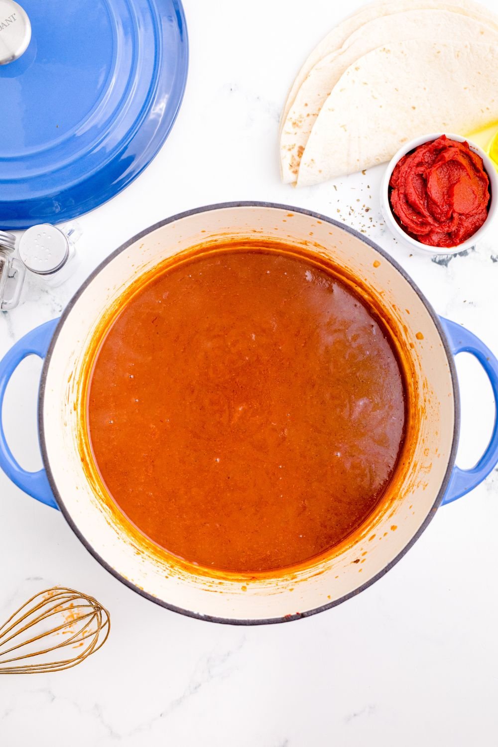 Homemade Enchilada Sauce in a pot sitting on table with whisk to the side of pan