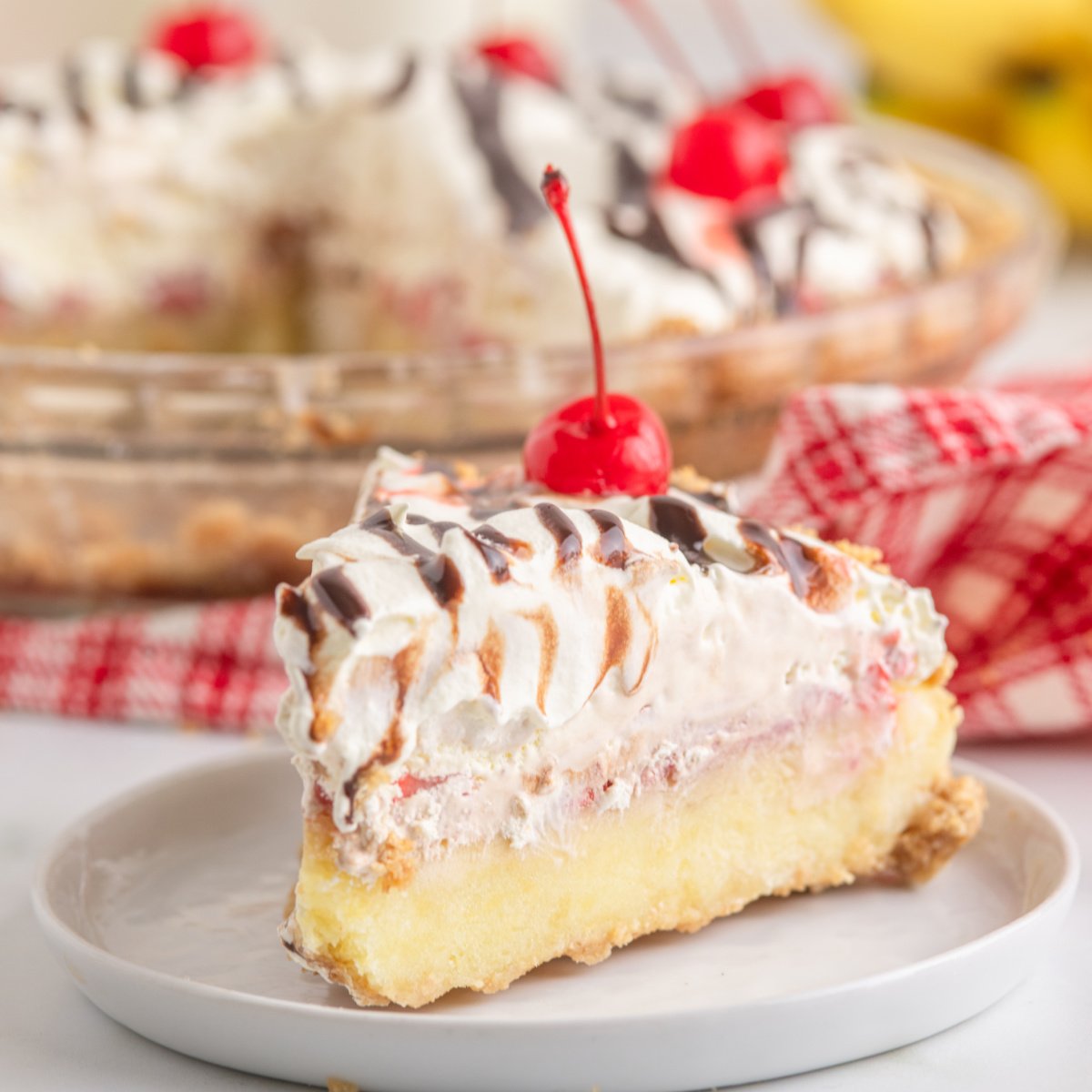No Bake Banana Split Pie on a white plate topped with a cherry and fudge drizzle