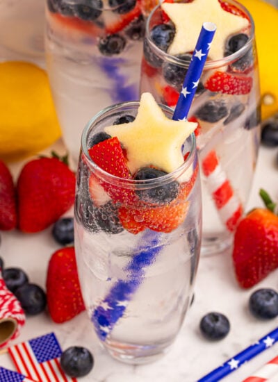 Patriotic Sparkling Lemonade in clear tall glasses on a white marble table surrounded by fresh fruit