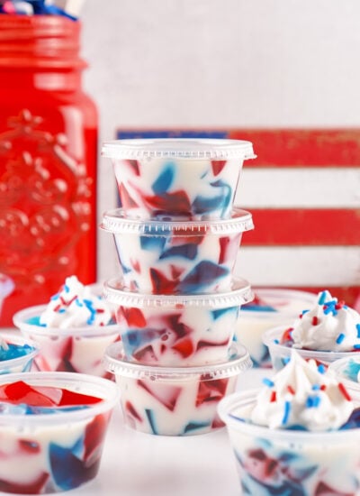 Red White and Blue Jello Shots in containers spread out on table with red white and blue decor in the background