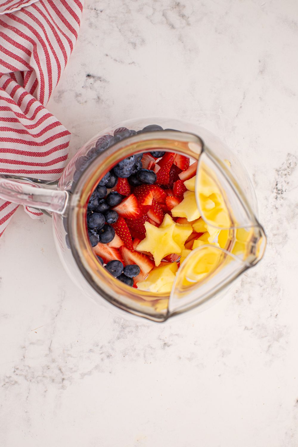 overhead look of pitcher with apples, blueberries, and strawberries
