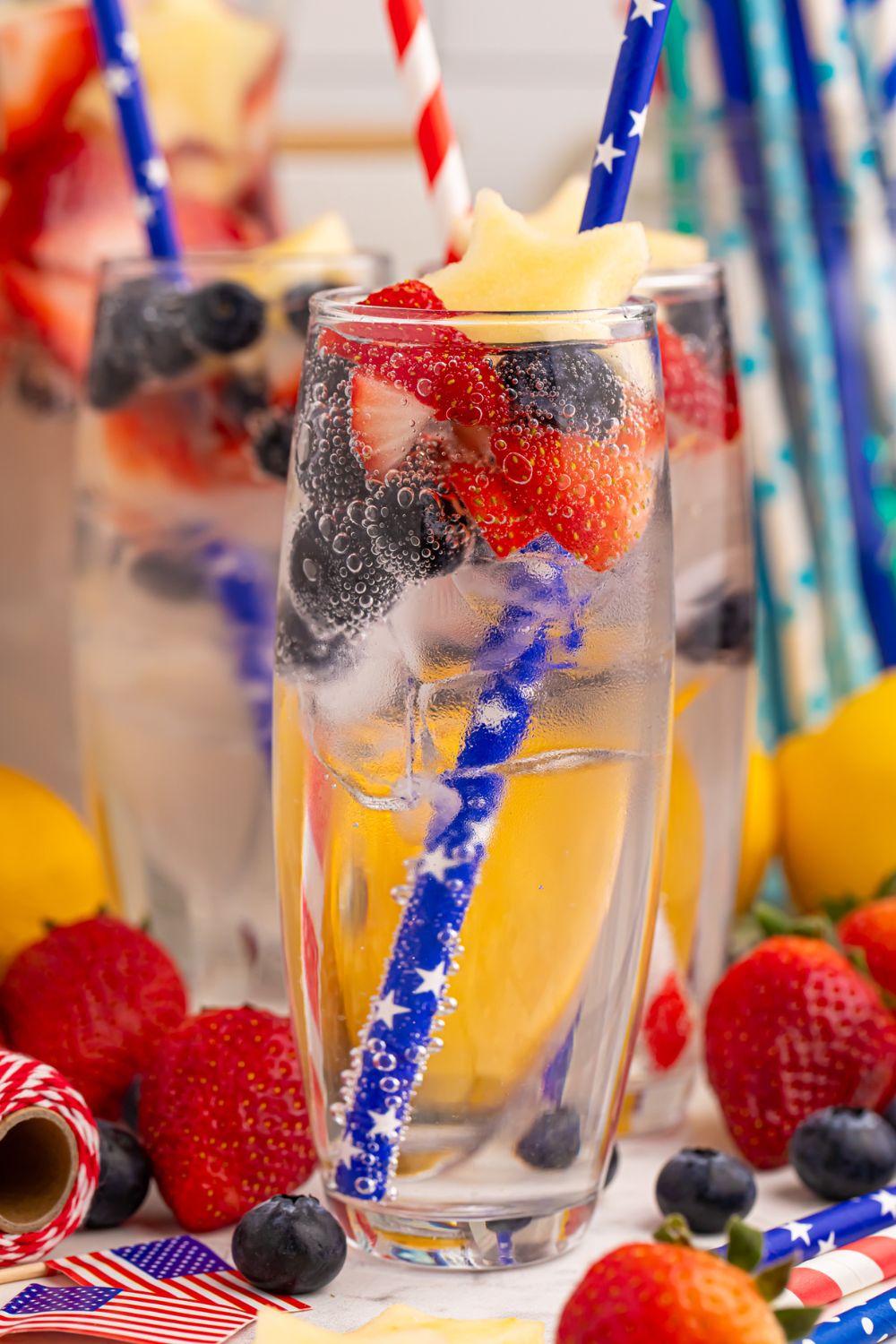 table with Fourth of July drinks with straws and fresh berries and apples in each glass
