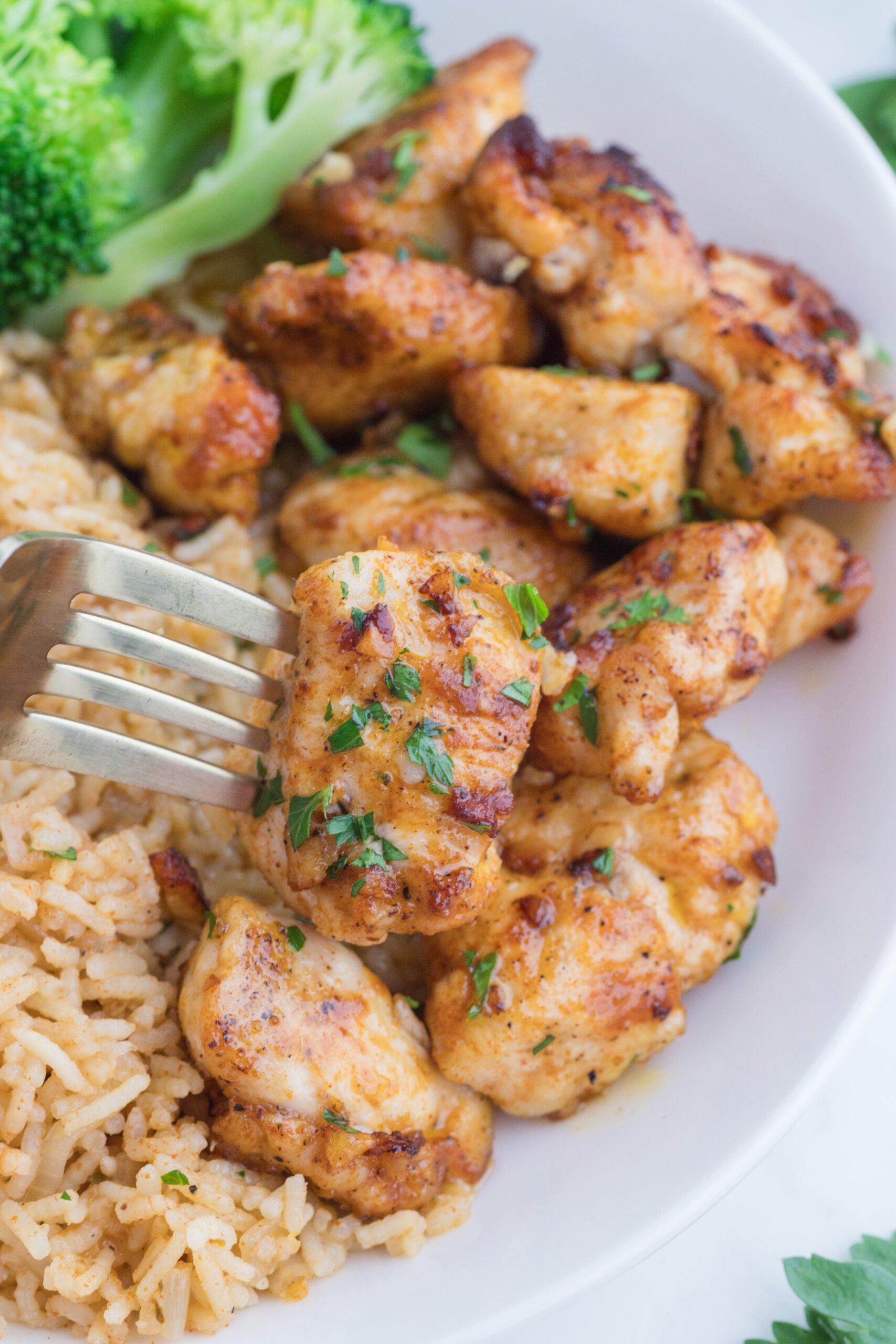 Garlic Butter Chicken Bites on a white plate with a fork lifting one up